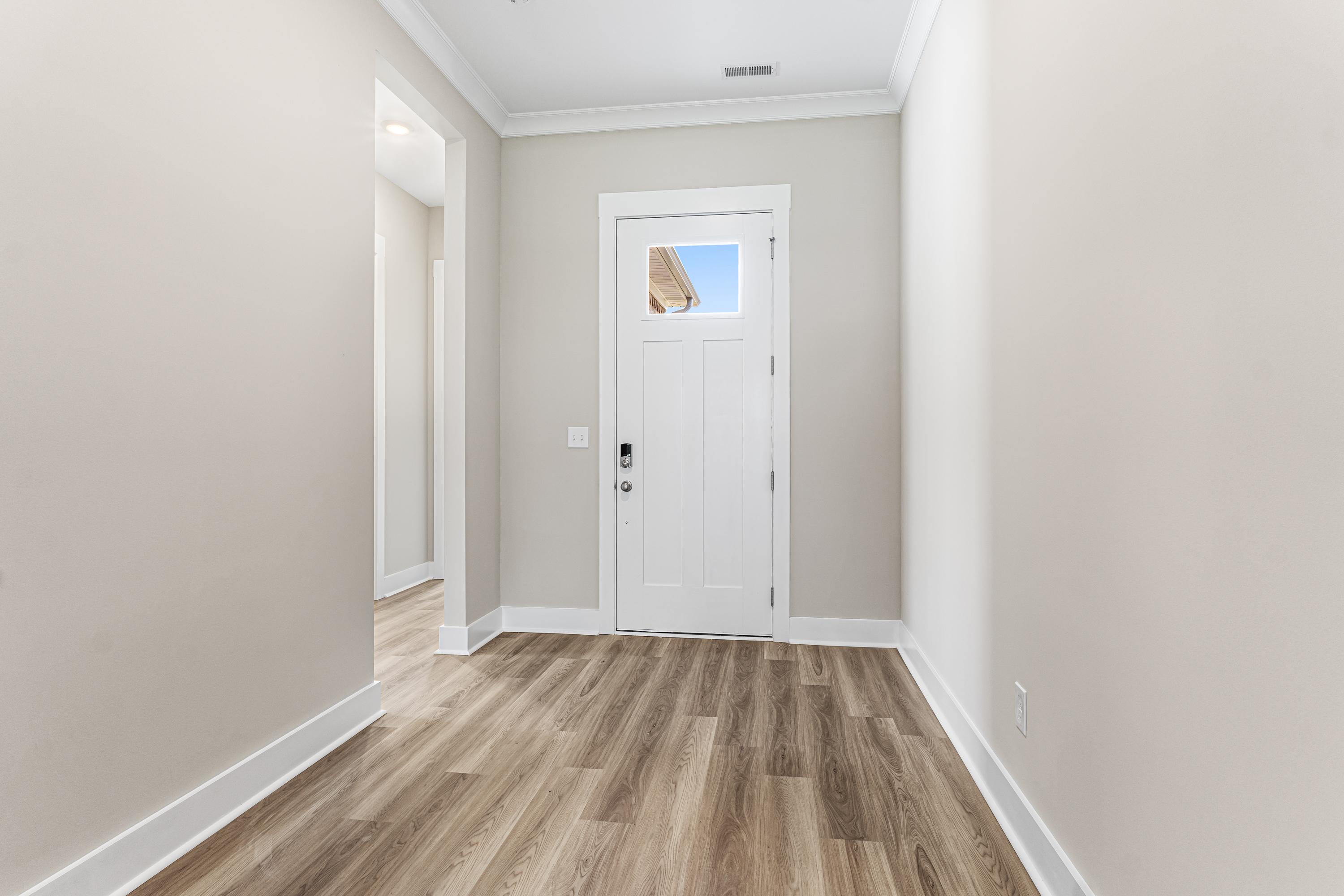 Spacious hallway in The Oxford A with beige walls, white paneled door, and light hardwood floors