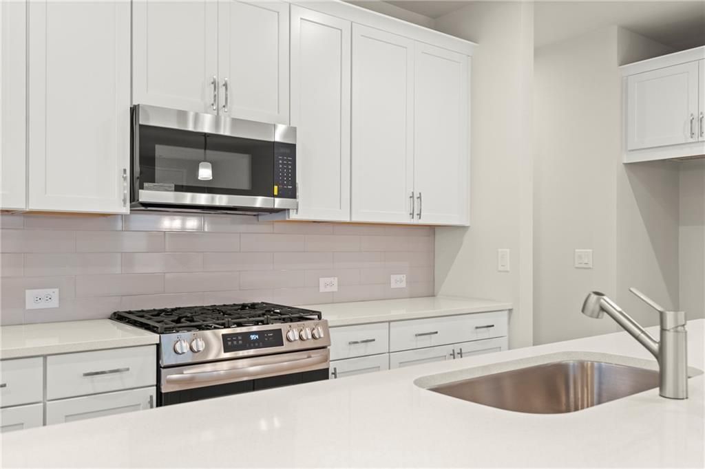 Modern white kitchen featuring stainless steel gas range, microwave, and quartz counters in Davidson Homes The Cary A, Kennesaw, GA