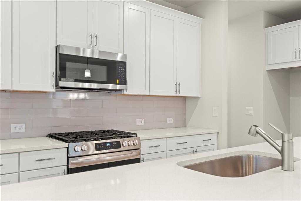 Modern white kitchen with stainless steel gas range, microwave, quartz counters, and pink subway tile backsplash in Davidson Homes The Cary A, Kennesaw, GA