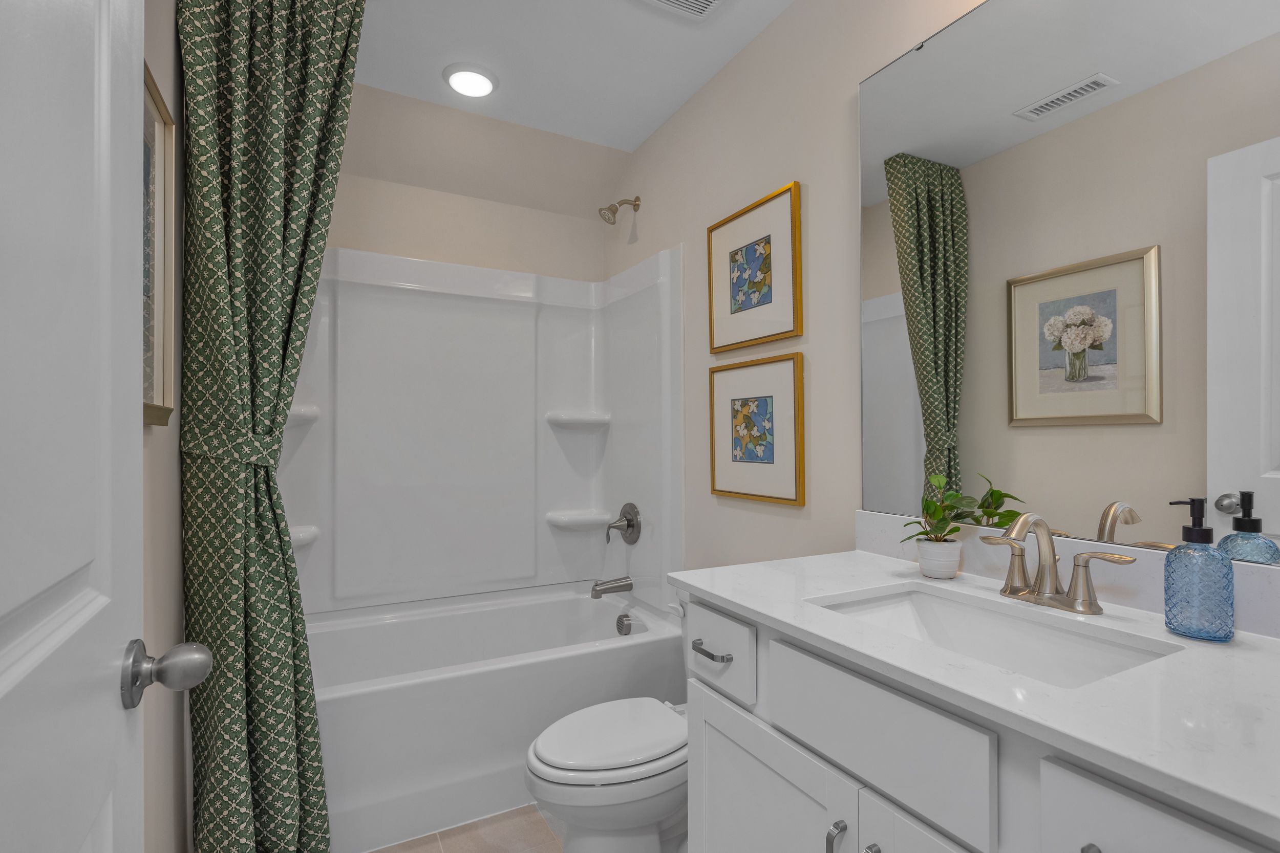 Elegant bathroom at Sage on North Main in Wake Forest NC with white bathtub, green patterned shower curtain, modern vanity and gold faucet