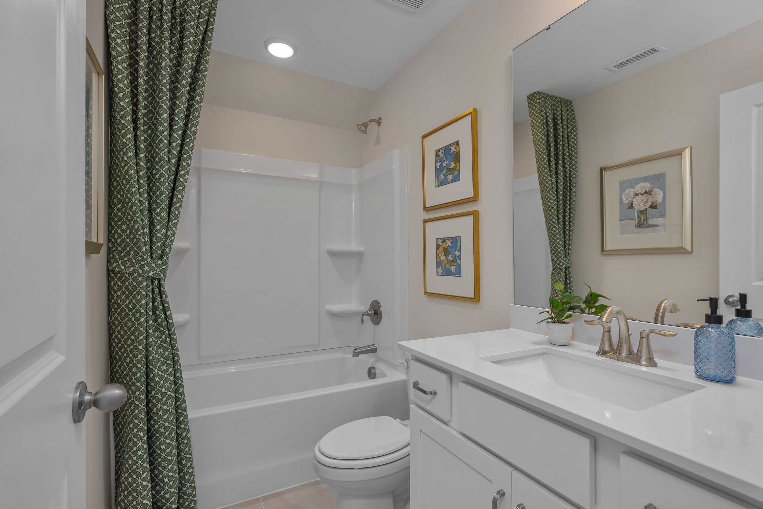 Elegant bathroom at Sage on North Main in Wake Forest NC with white bathtub, green patterned shower curtain, modern vanity and gold faucet