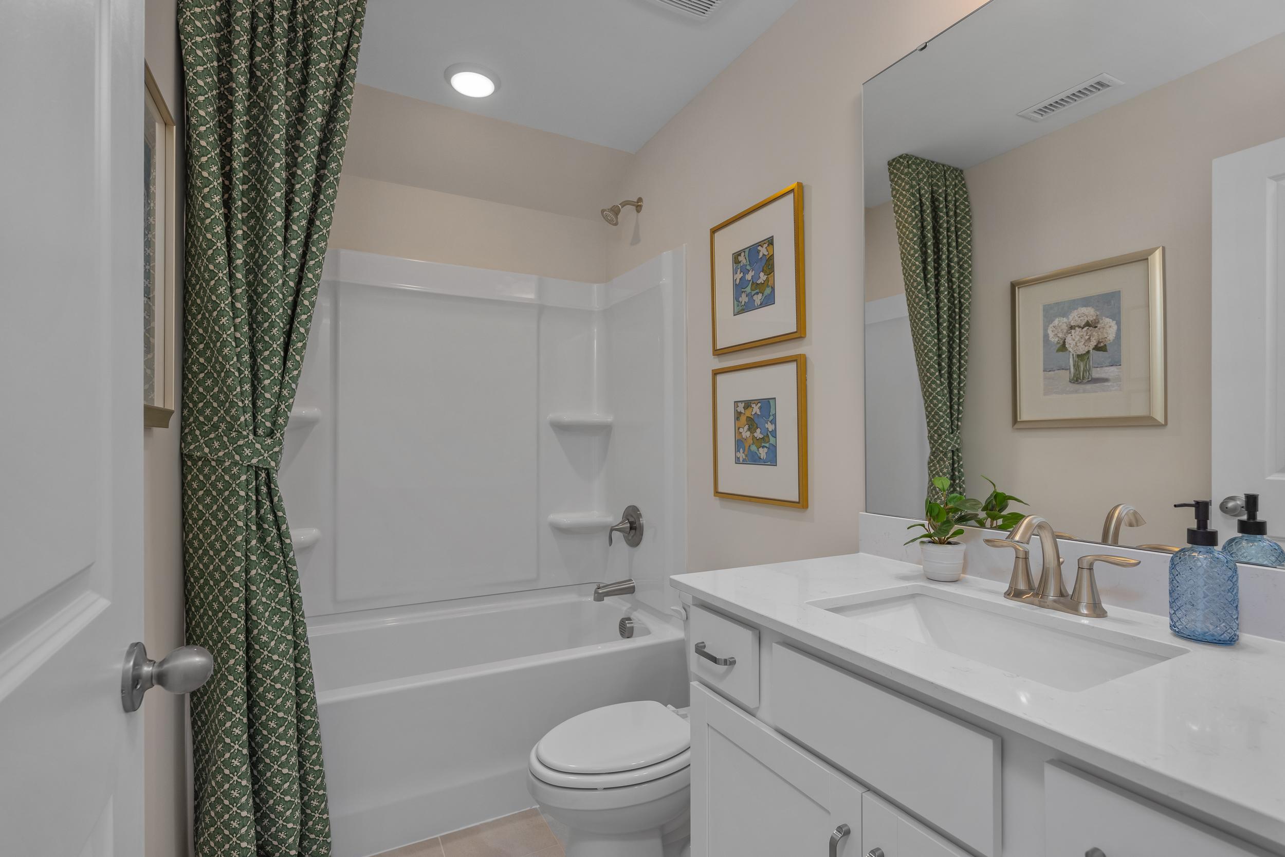 Elegant bathroom at Sage on North Main in Wake Forest NC with white bathtub, green patterned shower curtain, modern vanity and gold faucet
