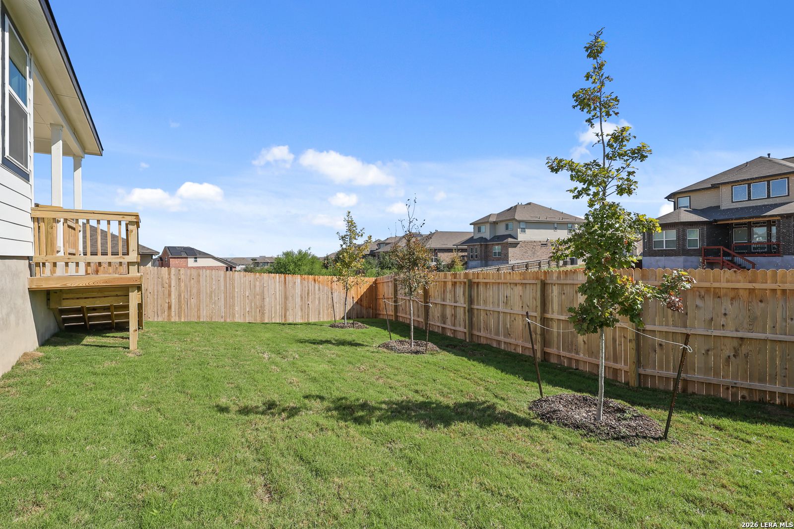 Fenced backyard with wooden deck and young trees at Davidson Homes The Glenwood E in Comanche Ridge, San Antonio, Texas