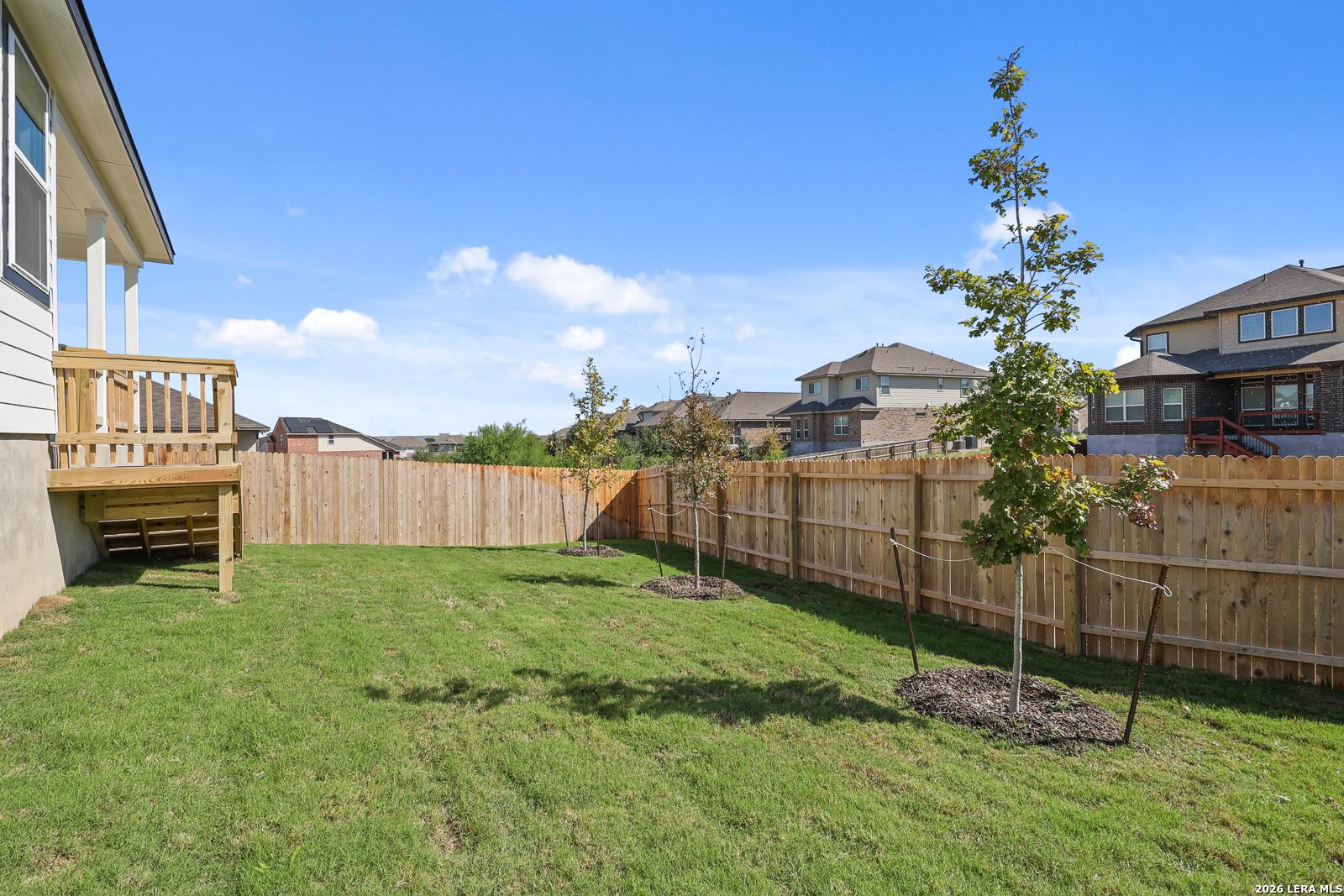 Fenced backyard with wooden deck and young trees at Davidson Homes The Glenwood E in Comanche Ridge, San Antonio, Texas