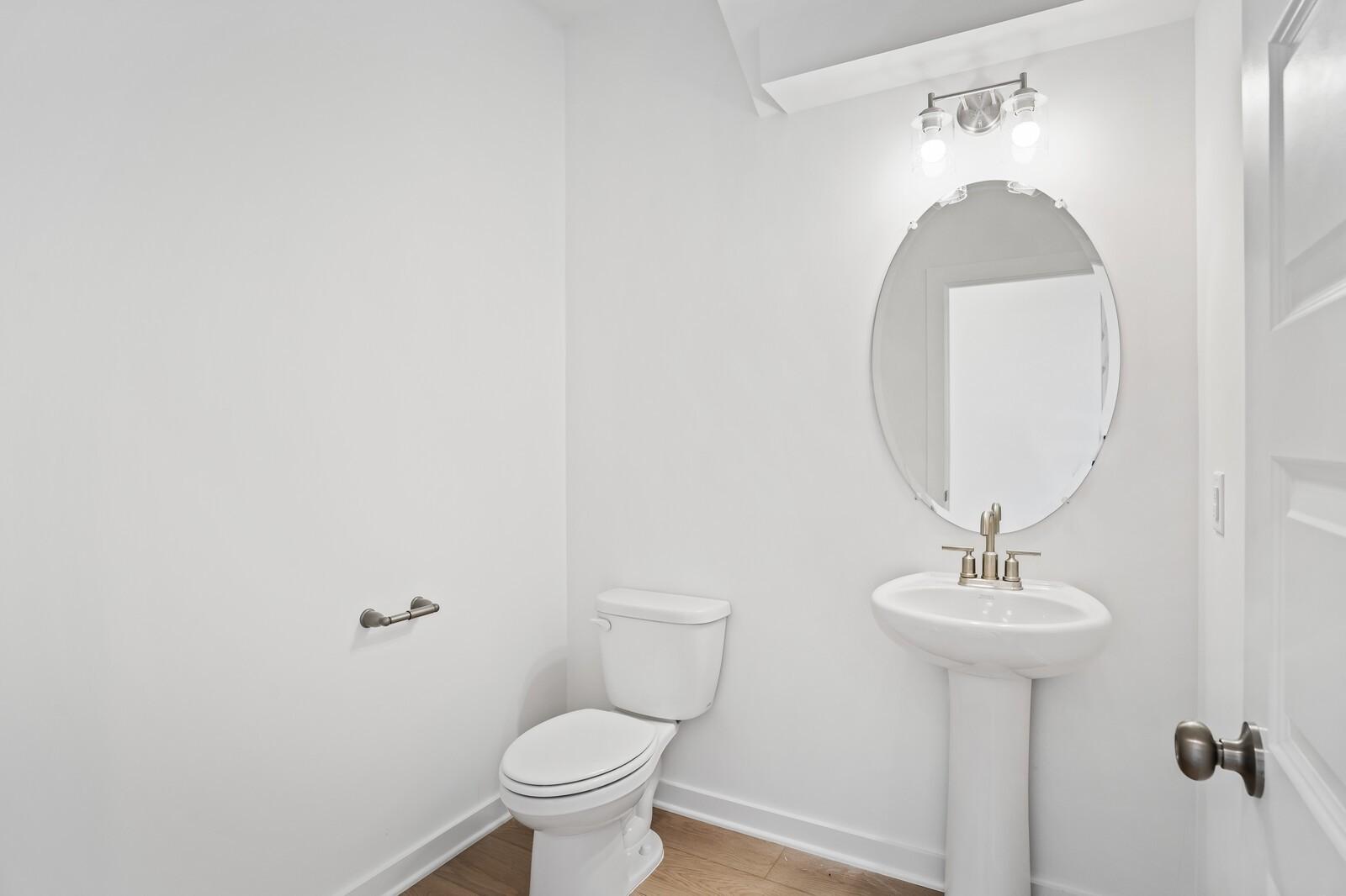 Bright powder room with pedestal sink, oval mirror, and modern lighting in The Logan C home at Calista Farms, Tennessee.