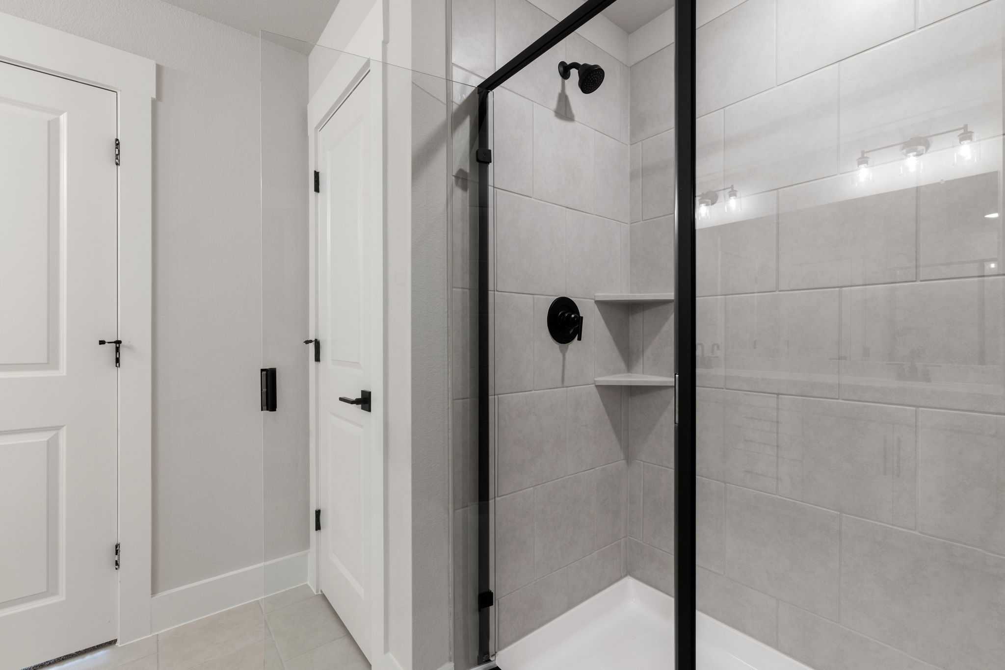 Modern frameless glass shower with white subway tiles, black fixtures, and niche in Davidson Homes The Durham E, Wylie, Texas