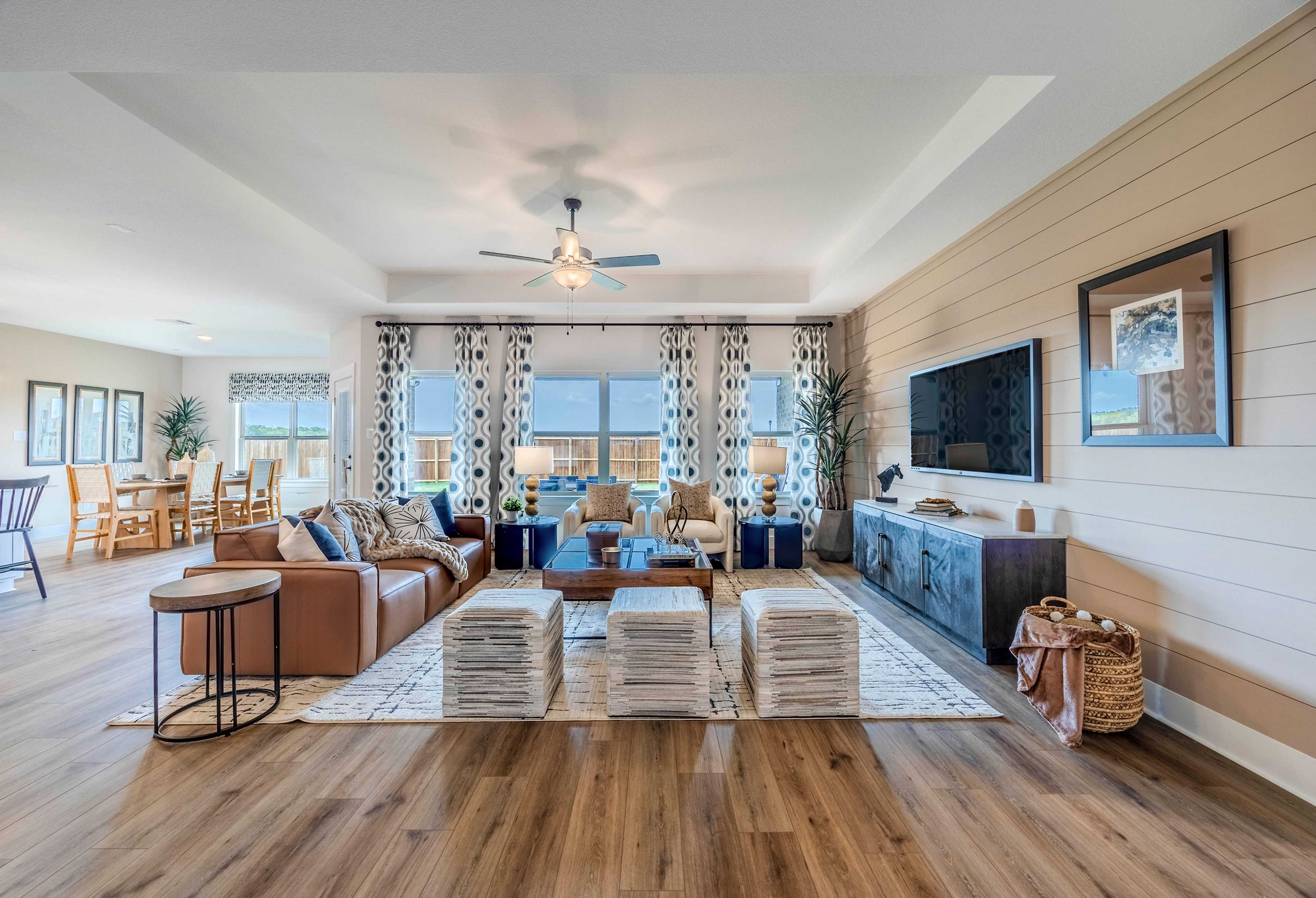 Spacious open-concept living room in The Rockford home with leather sectional, mounted TV on shiplap wall, dining area, and large windows
