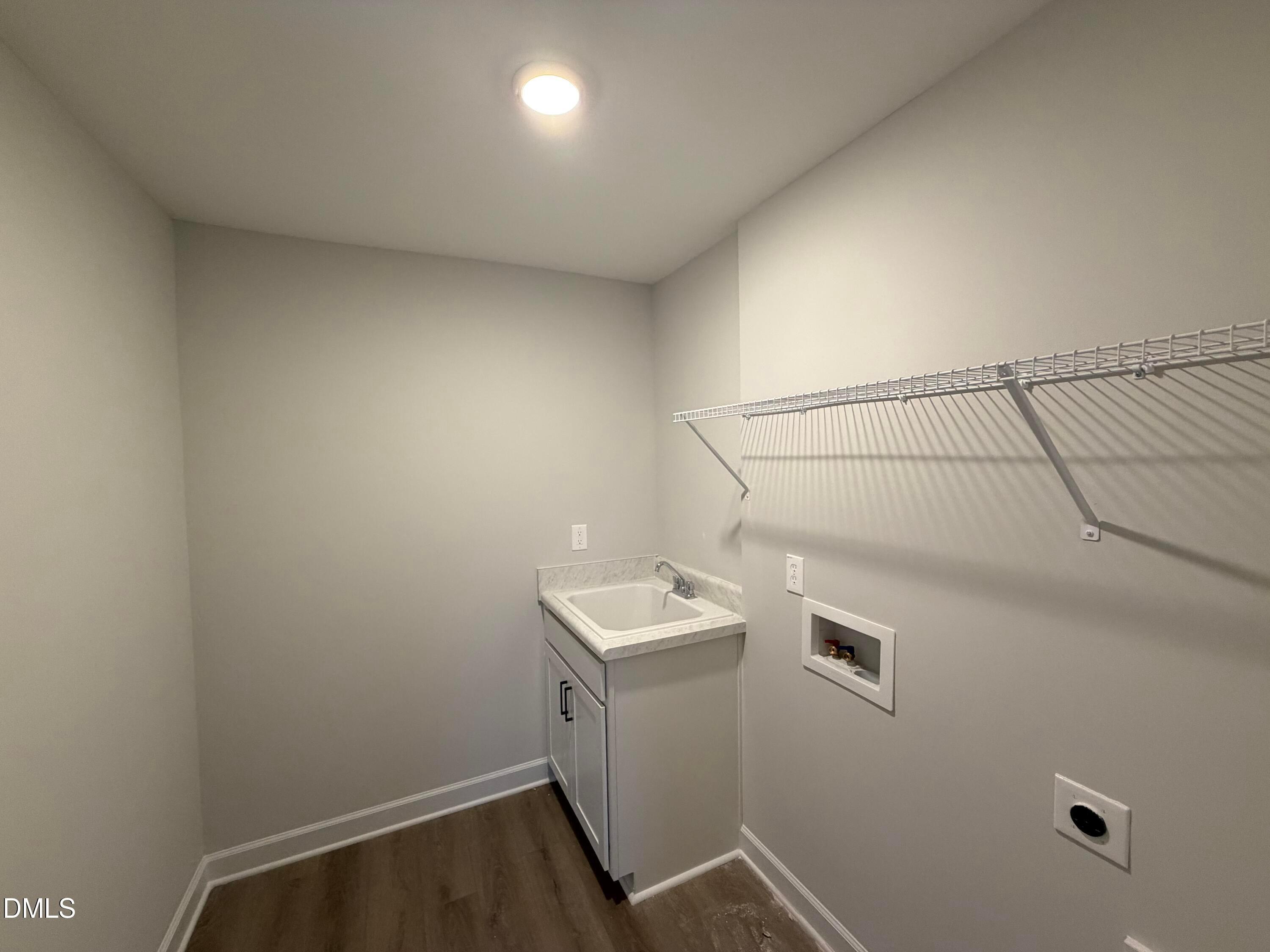 Laundry room with utility sink, white cabinetry, wire shelving, and wood-look flooring in Davidson Homes The Preston C, Wendell NC