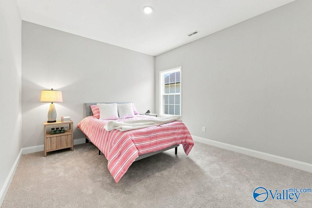 Bright bedroom with pink striped bedding, wood nightstand, and plush carpet in The Harrison floor plan, Hartselle, Alabama