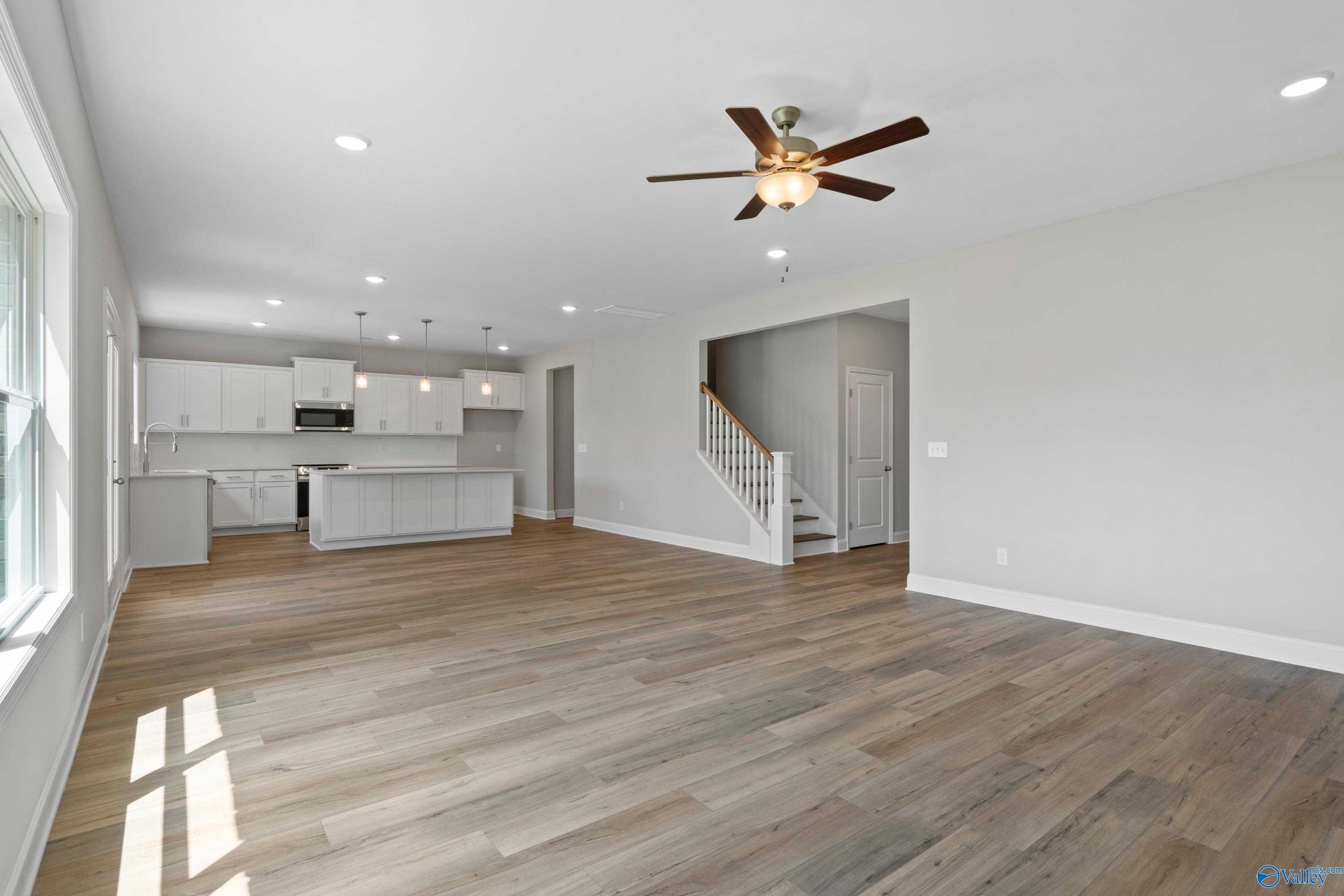 Spacious open-concept kitchen and living area with white cabinets, large island, hardwood floors, and staircase in Davidson Homes The Chelsea B, New Market, Alabama