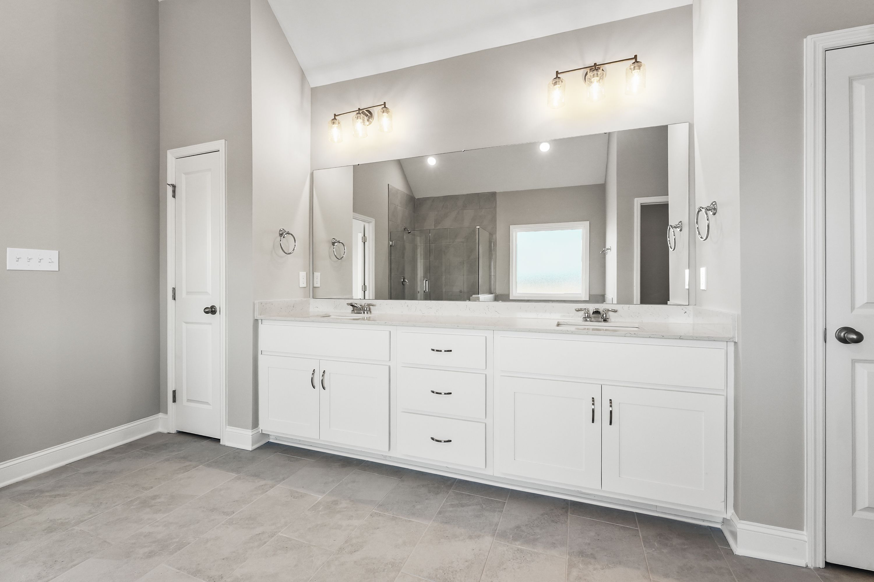 Spacious master bathroom in The Valencia with double white vanity, large mirror, and glass shower enclosure