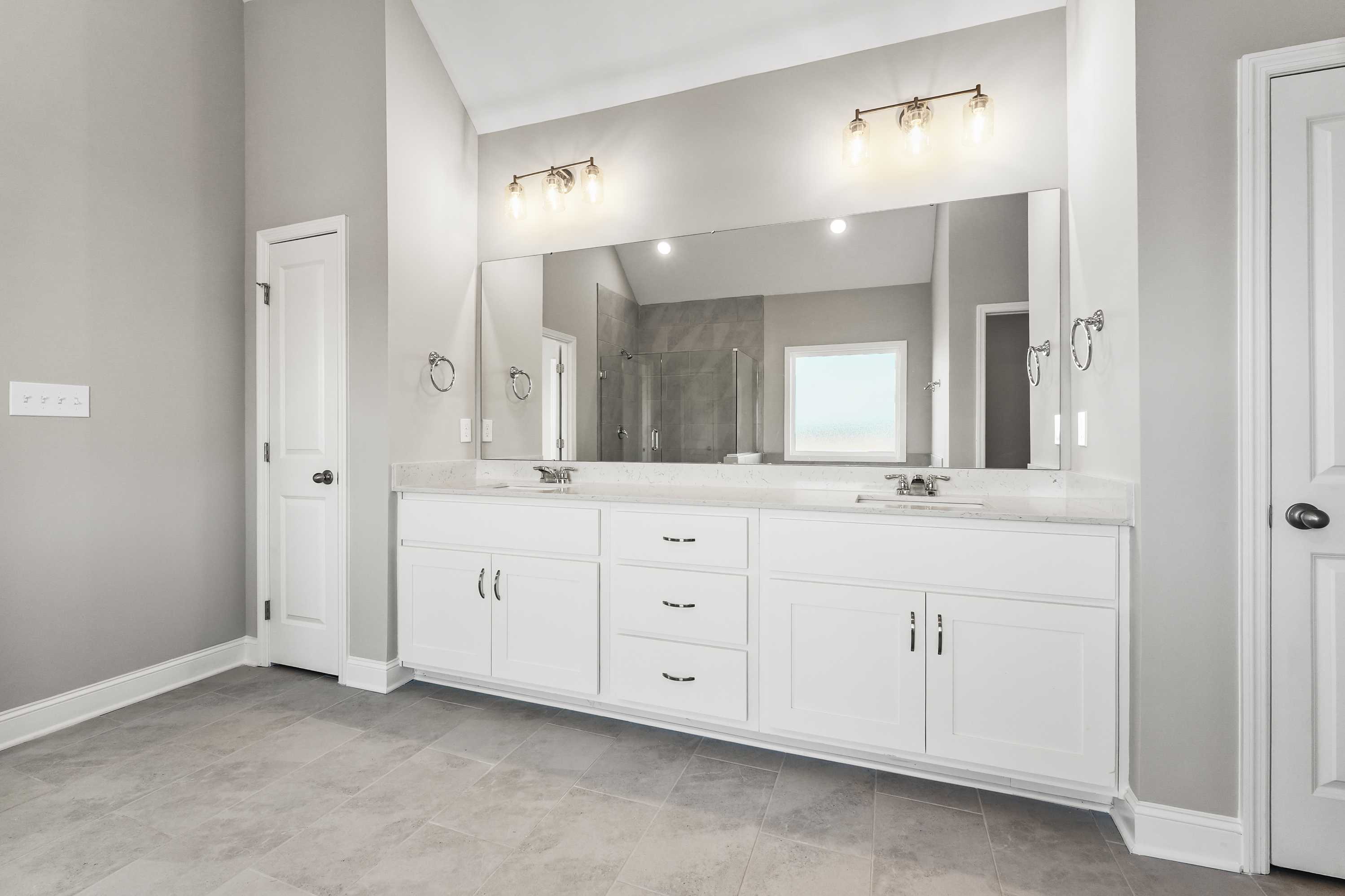 Spacious master bathroom in The Valencia with double white vanity, large mirror, and glass shower enclosure