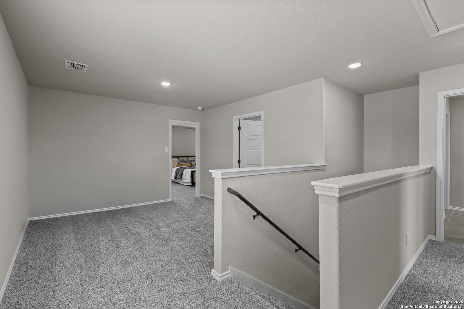 Spacious upstairs hallway with gray carpet, white balustrades, and bedroom doors in Davidson Homes The Charlotte B, San Antonio