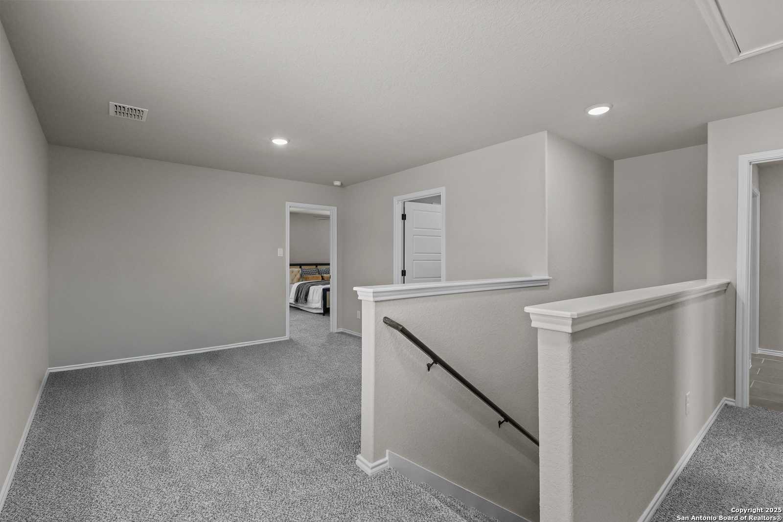 Spacious upstairs hallway with gray carpet, white balustrades, and bedroom doors in Davidson Homes The Charlotte B, San Antonio