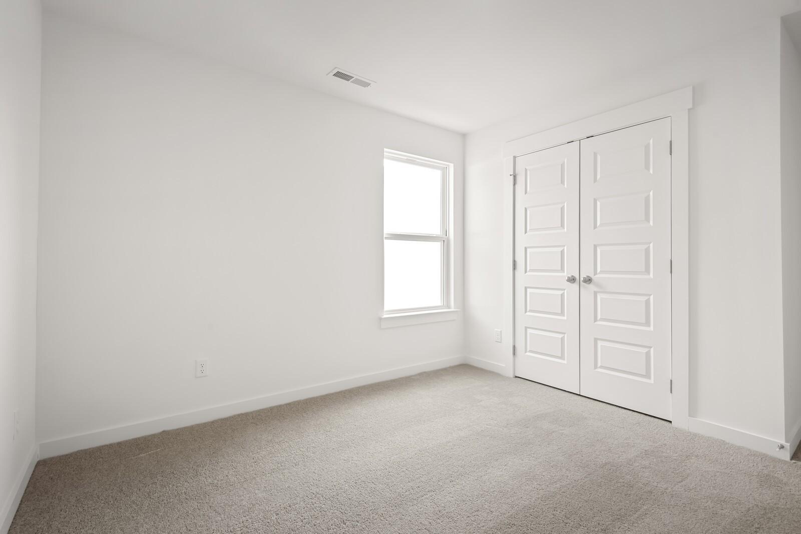 Bright secondary bedroom with double closet doors, large window, and neutral carpet in Davidson Homes The Logan C, Gallatin, TN