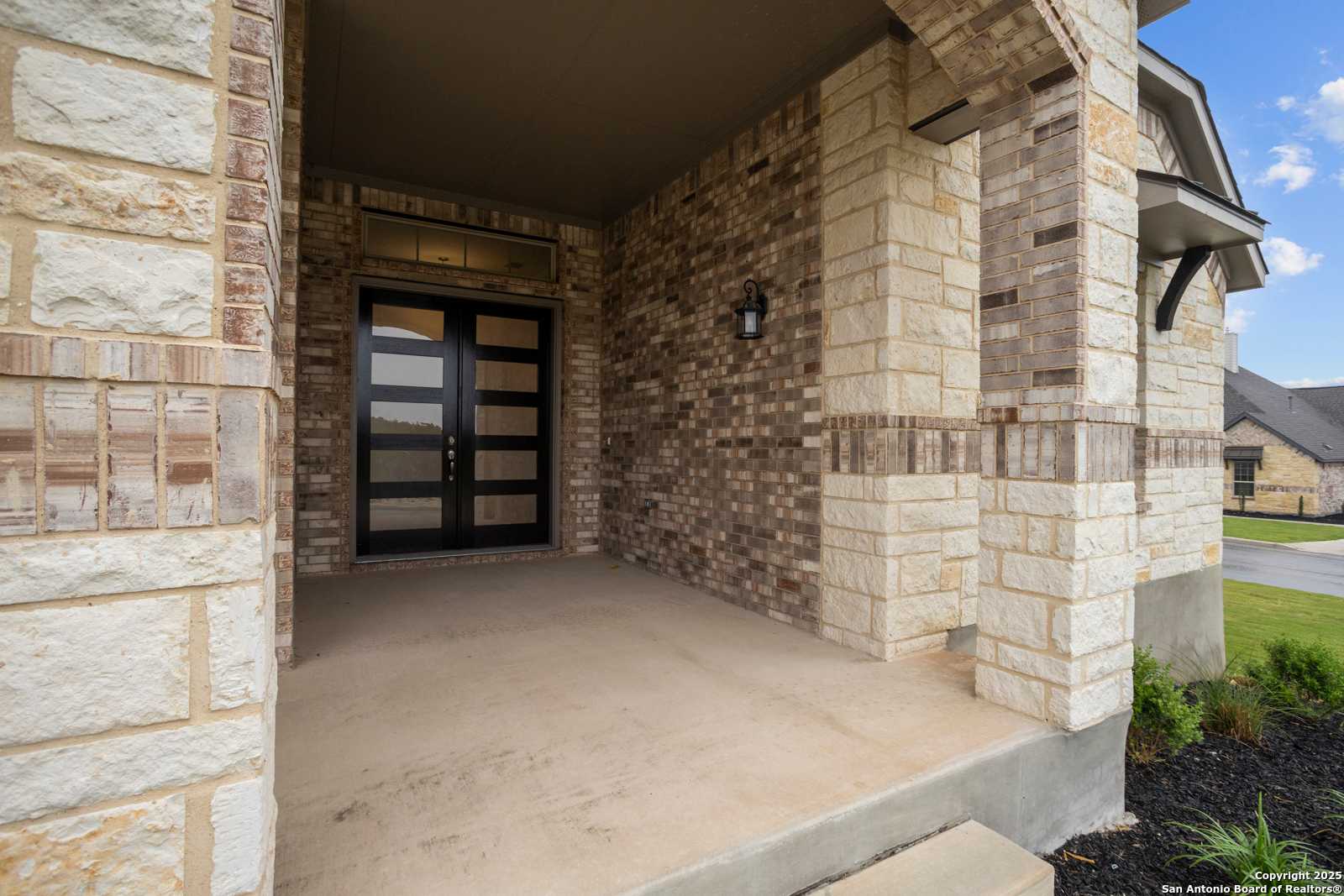 Modern glass double doors on covered front porch with stone and brick facade in Davidson Homes The Summerlin B, Castroville, Texas