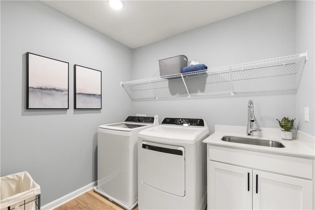 Modern laundry room with white washer-dryer, utility sink, wire shelves, abstract art in The Burton C by Davidson Homes, Canton GA