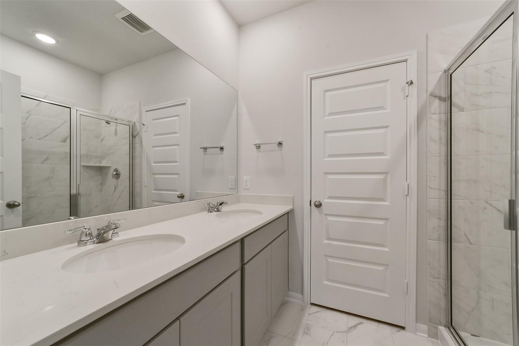 Modern master bathroom featuring double quartz vanity, frameless glass shower, and hexagon tile floor in Davidson Homes San Marcos E, Beasley, Texas