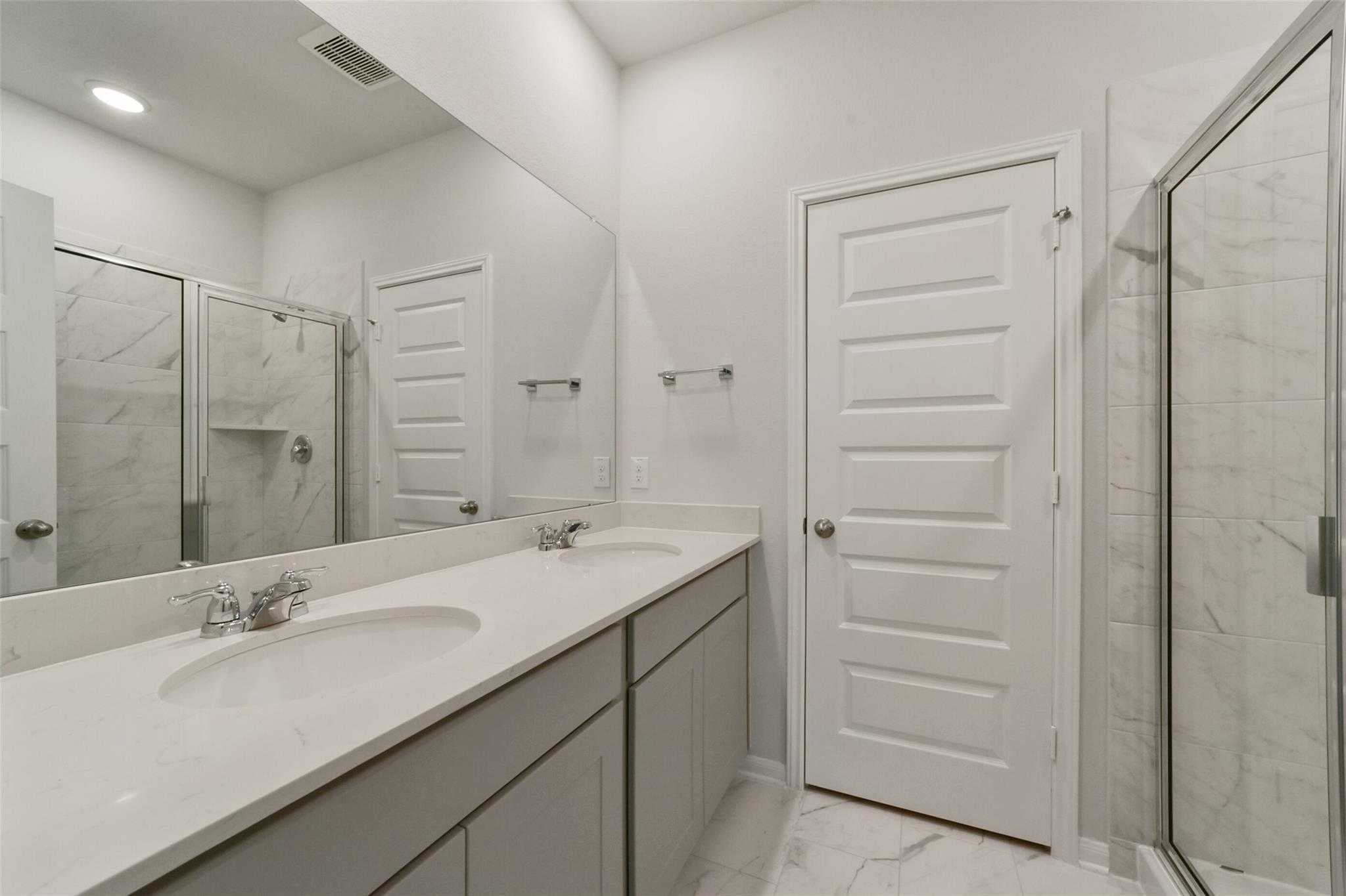 Modern master bathroom featuring double quartz vanity, frameless glass shower, and hexagon tile floor in Davidson Homes San Marcos E, Beasley, Texas