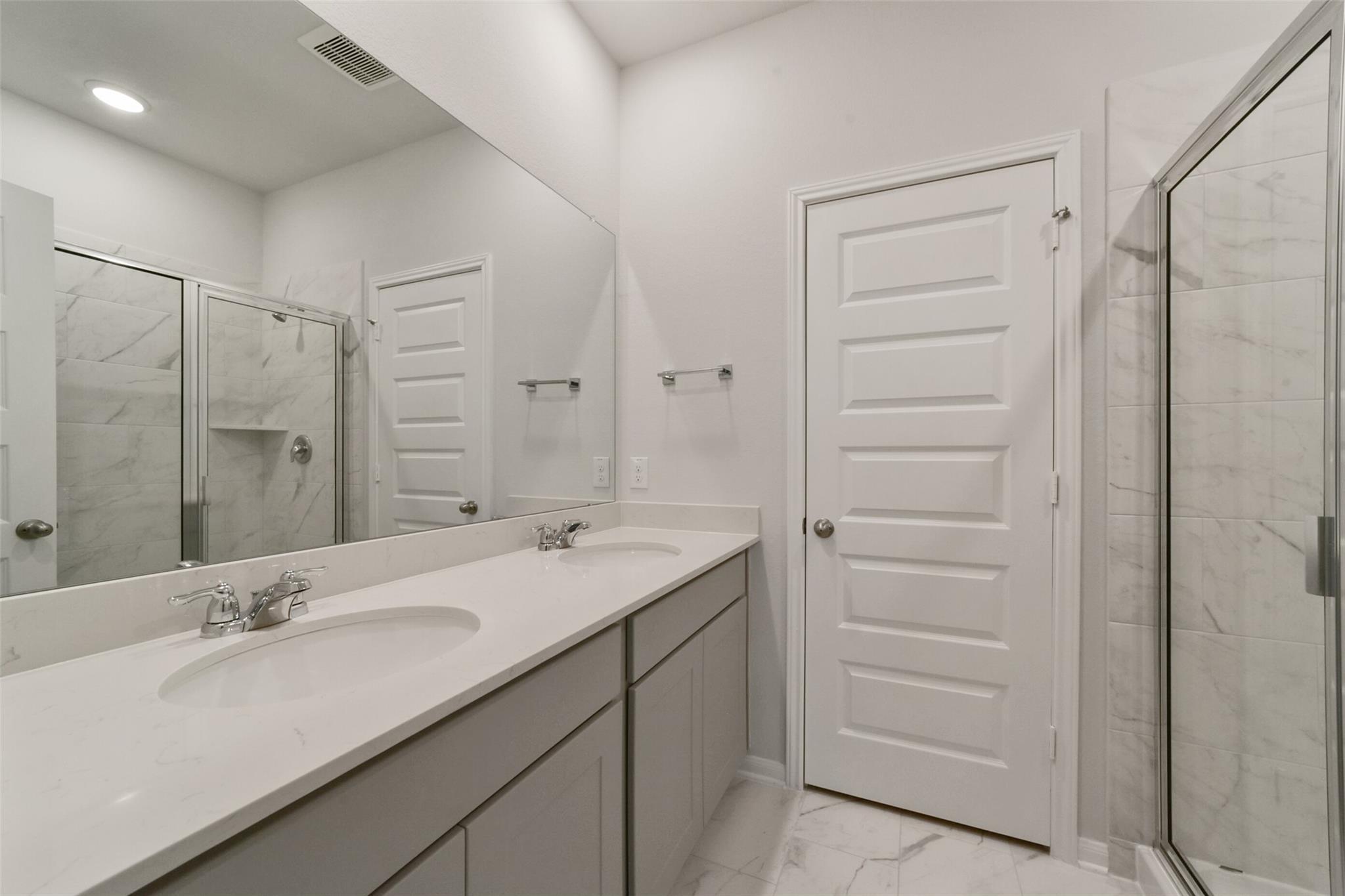 Modern master bathroom featuring double quartz vanity, frameless glass shower, and white subway tile in Davidson Homes San Marcos E, Beasley, Texas
