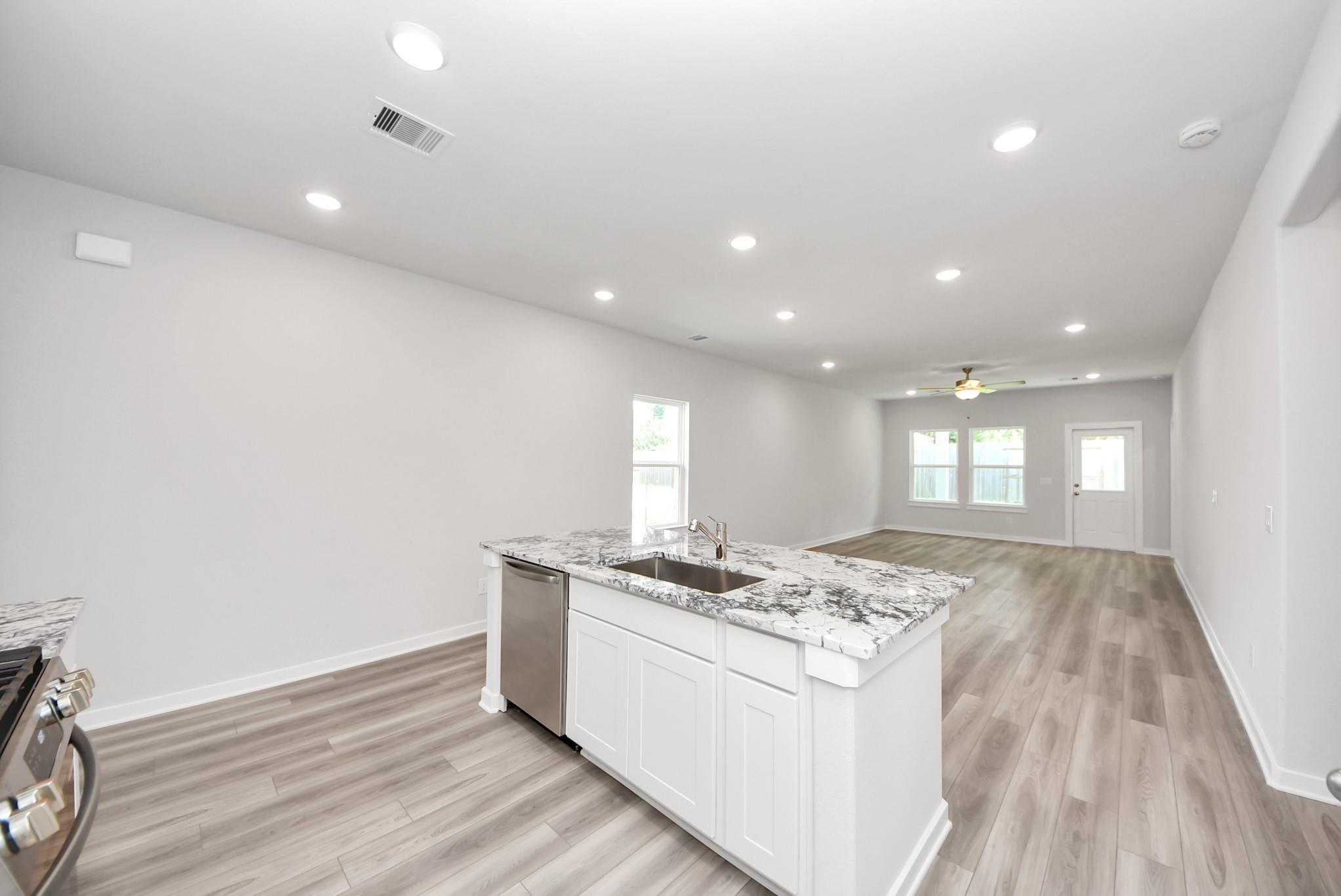 Open-concept kitchen with granite island and white cabinets in The Sabine E floor plan at Windmill Estates, Magnolia, TX.