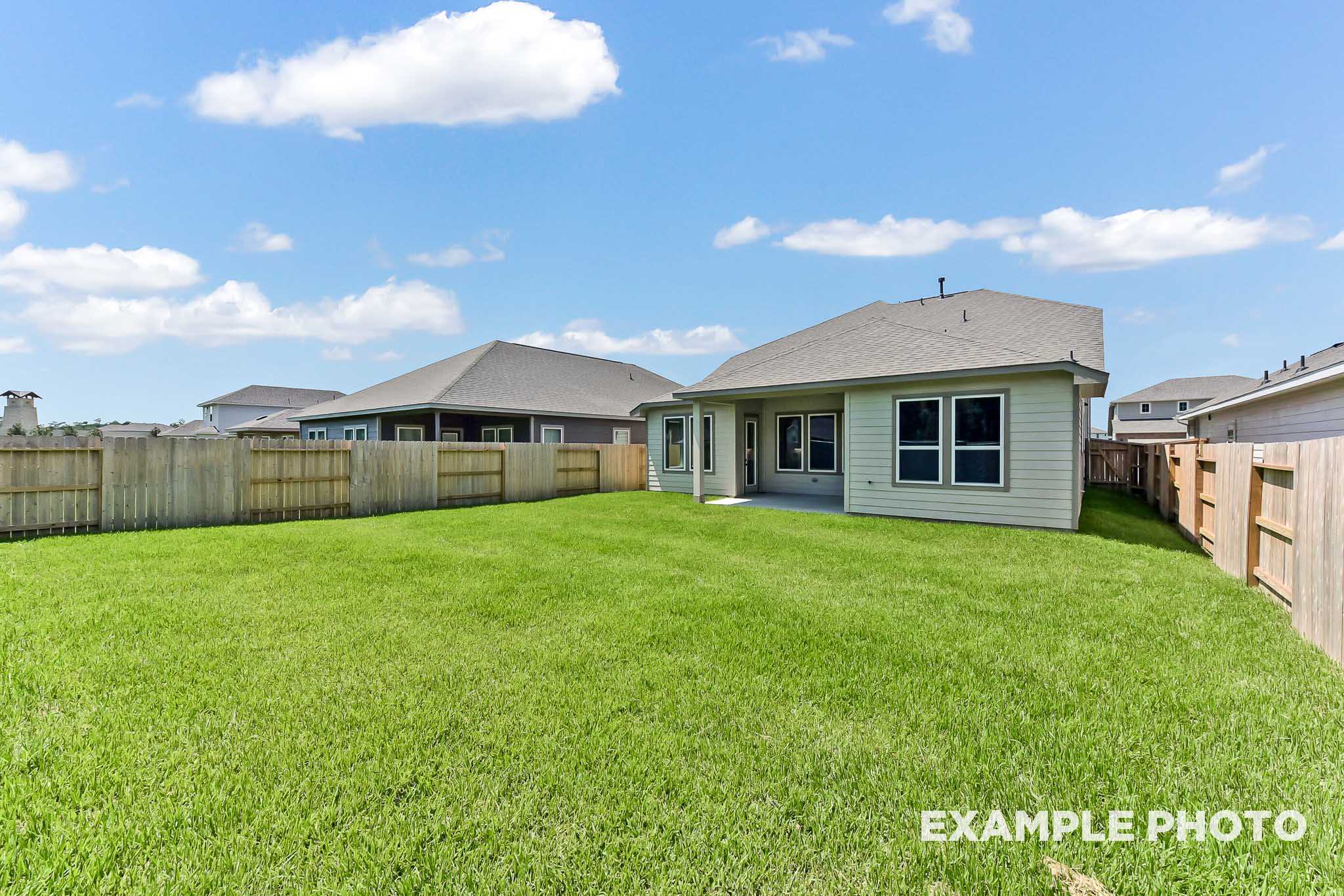 Spacious backyard of The Sequoia two-story home with covered patio, sliding doors, lush green lawn, and privacy fence in Crosby Texas