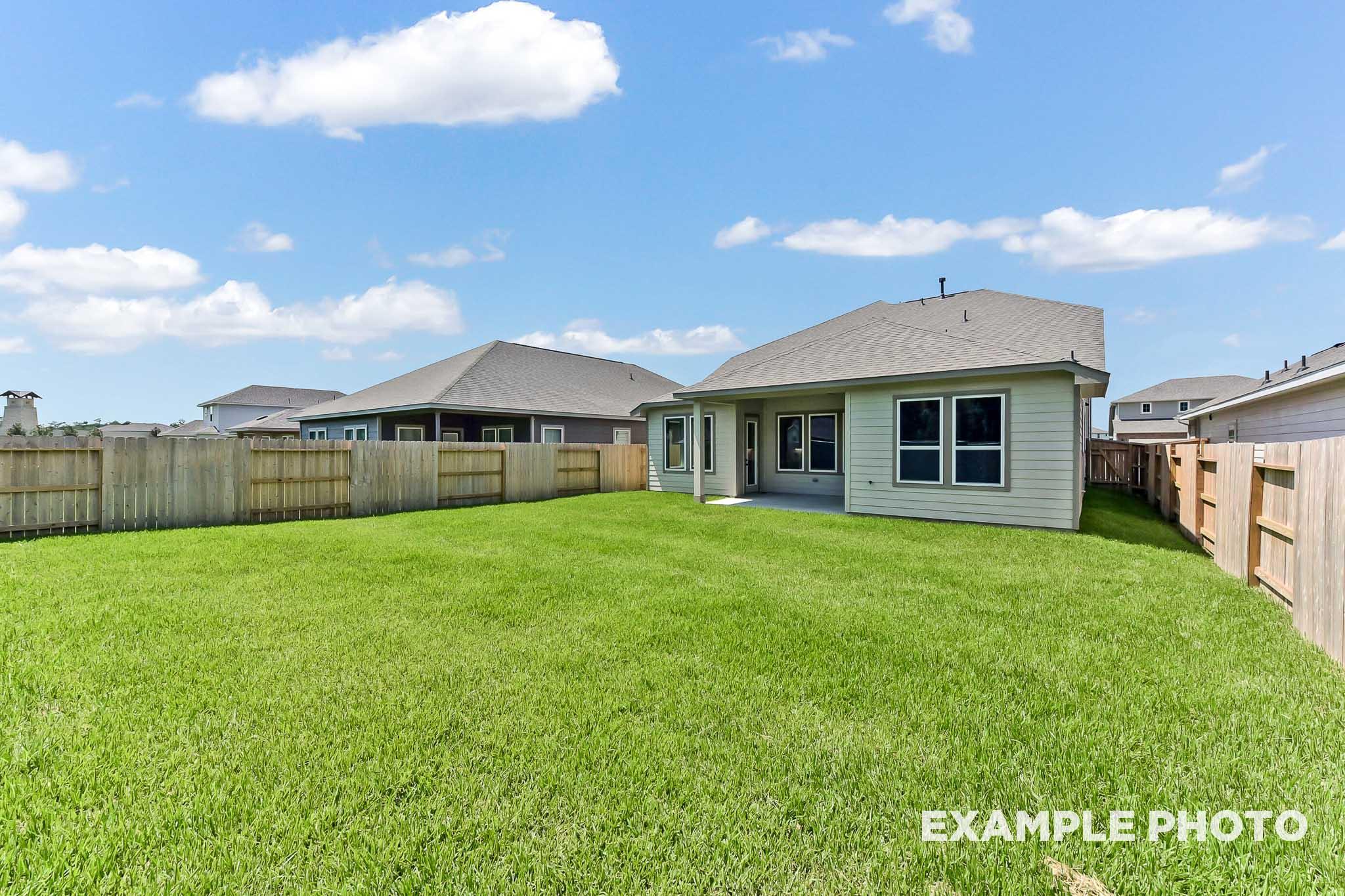 Spacious backyard of The Sequoia two-story home with covered patio, sliding doors, lush green lawn, and privacy fence in Crosby Texas