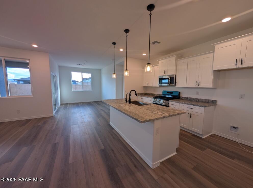 Open-concept kitchen with granite island, white shaker cabinets, pendant lights, and luxury vinyl plank flooring in The Newport A, Prescott