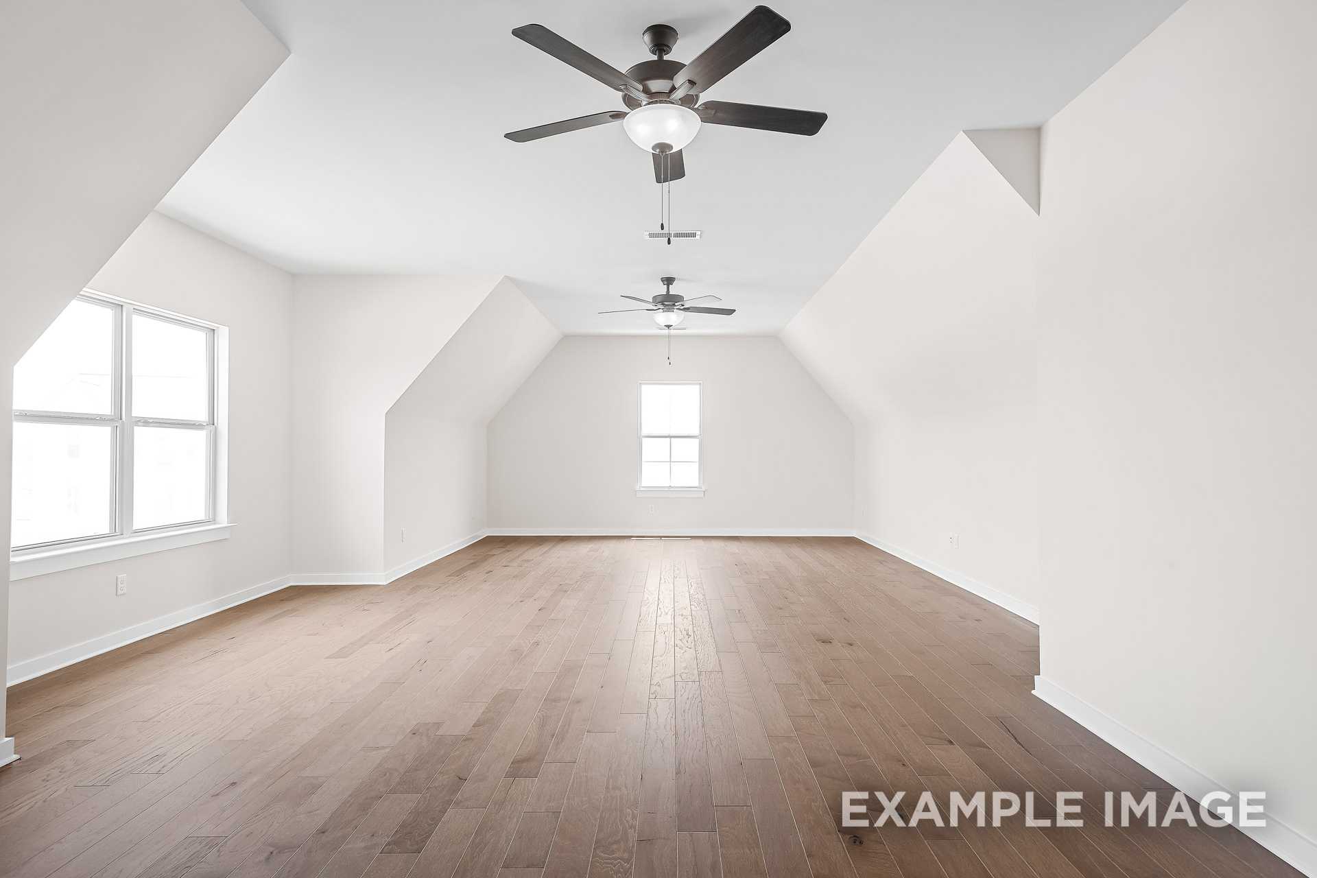Spacious bonus room in The Hawkins with vaulted white ceilings, dual ceiling fans, large windows, and hardwood floors