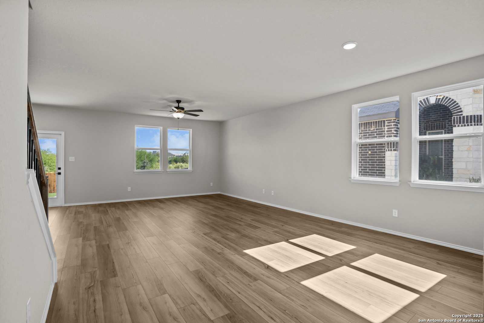 Spacious living room with hardwood floors, ceiling fan, and large windows in Davidson Homes The Murray F, Horizon Pointe, Converse, Texas