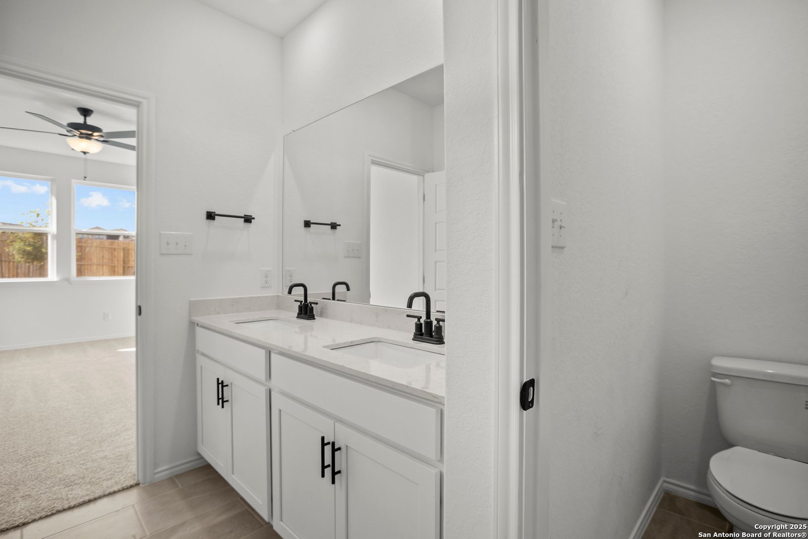 Modern double vanity with dual sinks, mirrors, and adjacent toilet in Davidson Homes The Daphne K, San Antonio, Texas