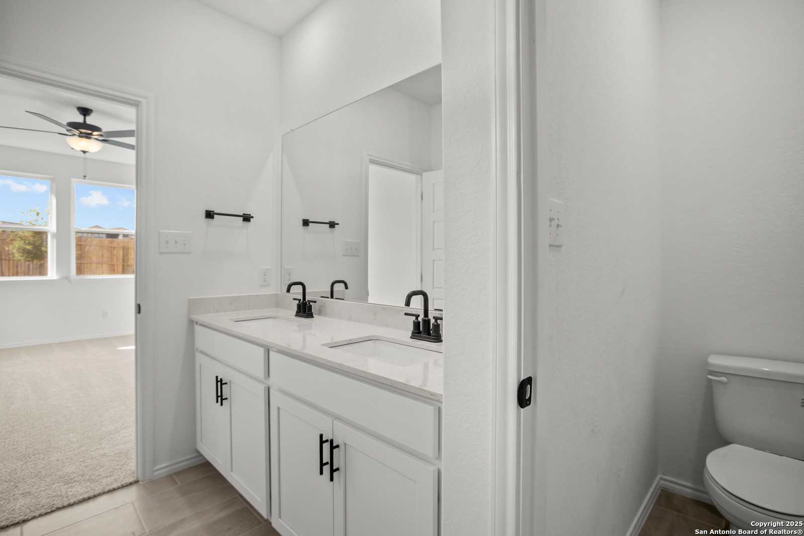 Modern double vanity with dual sinks, mirrors, and adjacent toilet in Davidson Homes The Daphne K, San Antonio, Texas