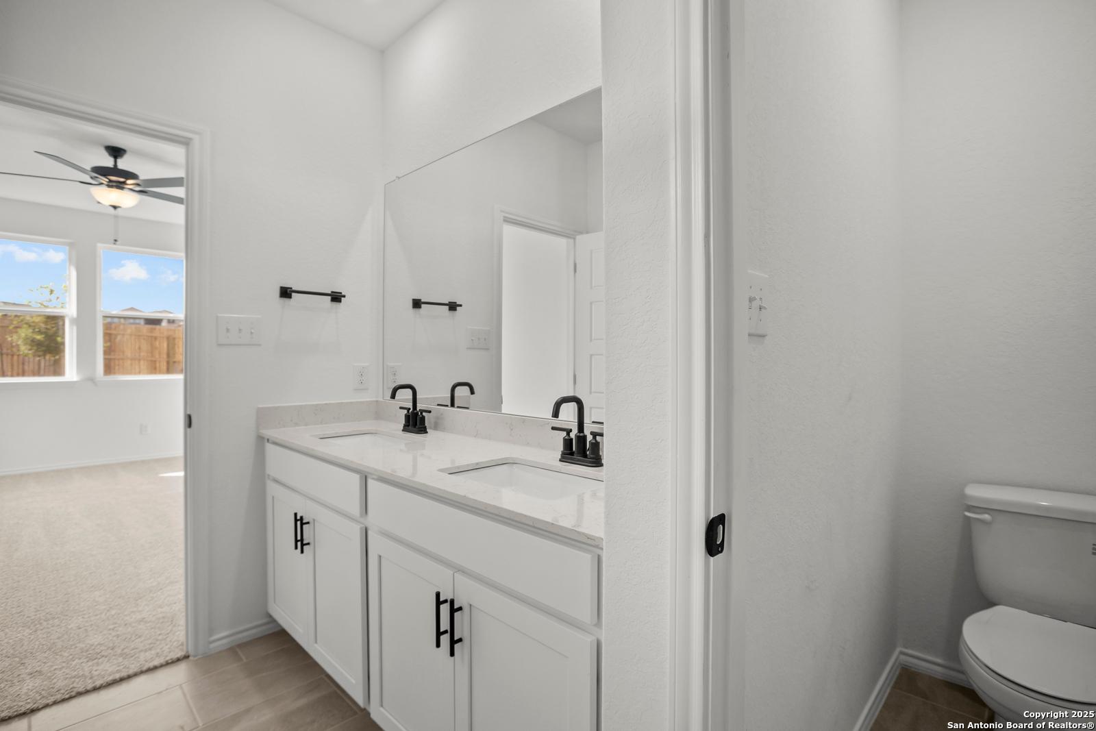 Modern double vanity with dual sinks, mirrors, and adjacent toilet in Davidson Homes The Daphne K, San Antonio, Texas