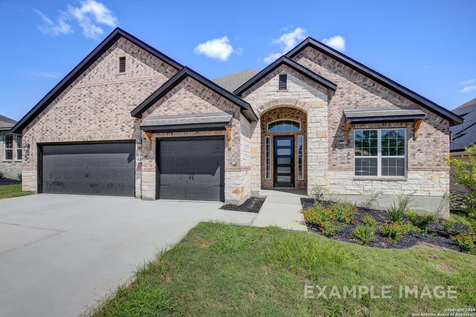 Modern brick ranch exterior with 3-car garage, stone arched entry, and lush landscaping in Castroville, Texas
