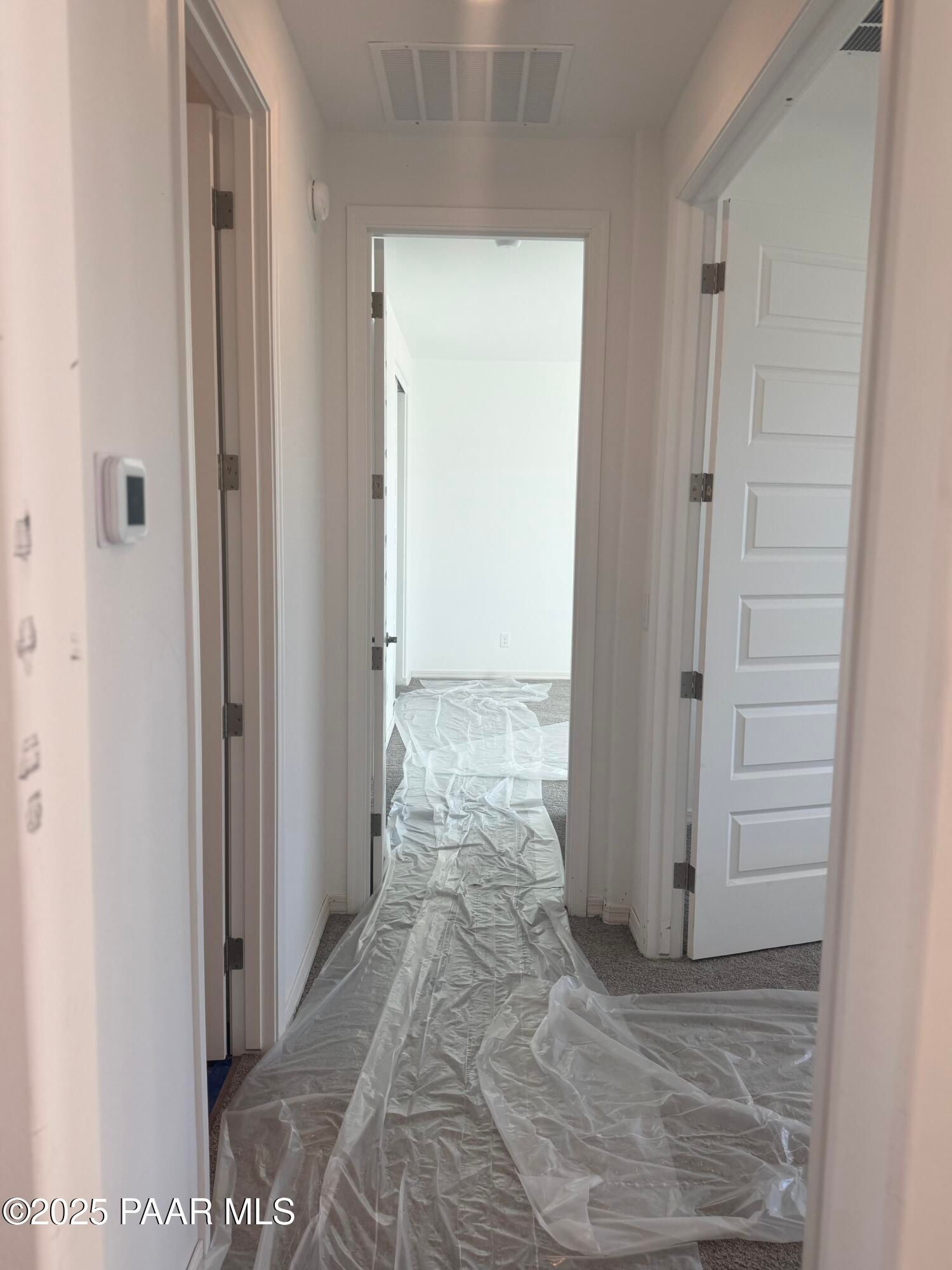 Bright hallway with open white doors and protective plastic sheeting on floor in Davidson Homes The Summit A, Prescott, Arizona