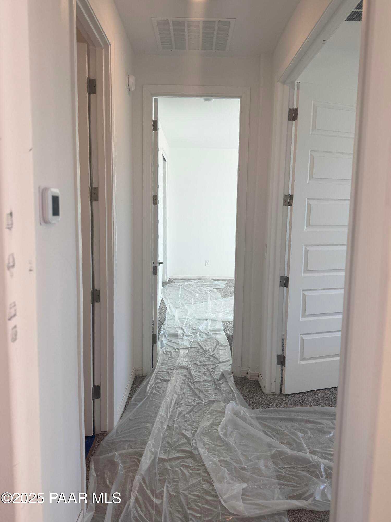 Bright hallway with open white doors and protective plastic sheeting on floor in Davidson Homes The Summit A, Prescott, Arizona