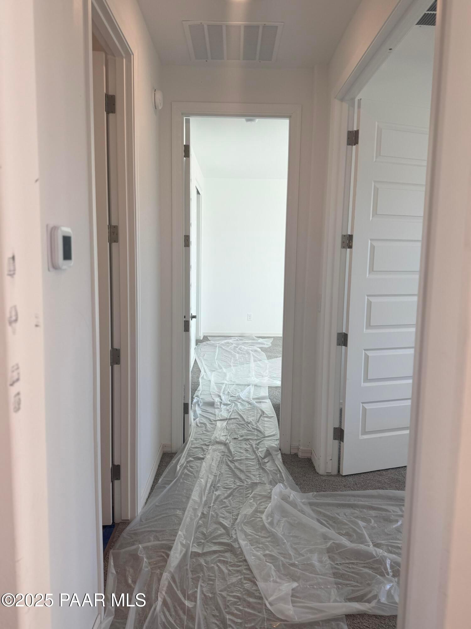 Bright hallway with open white doors and protective plastic sheeting on floor in Davidson Homes The Summit A, Prescott, Arizona