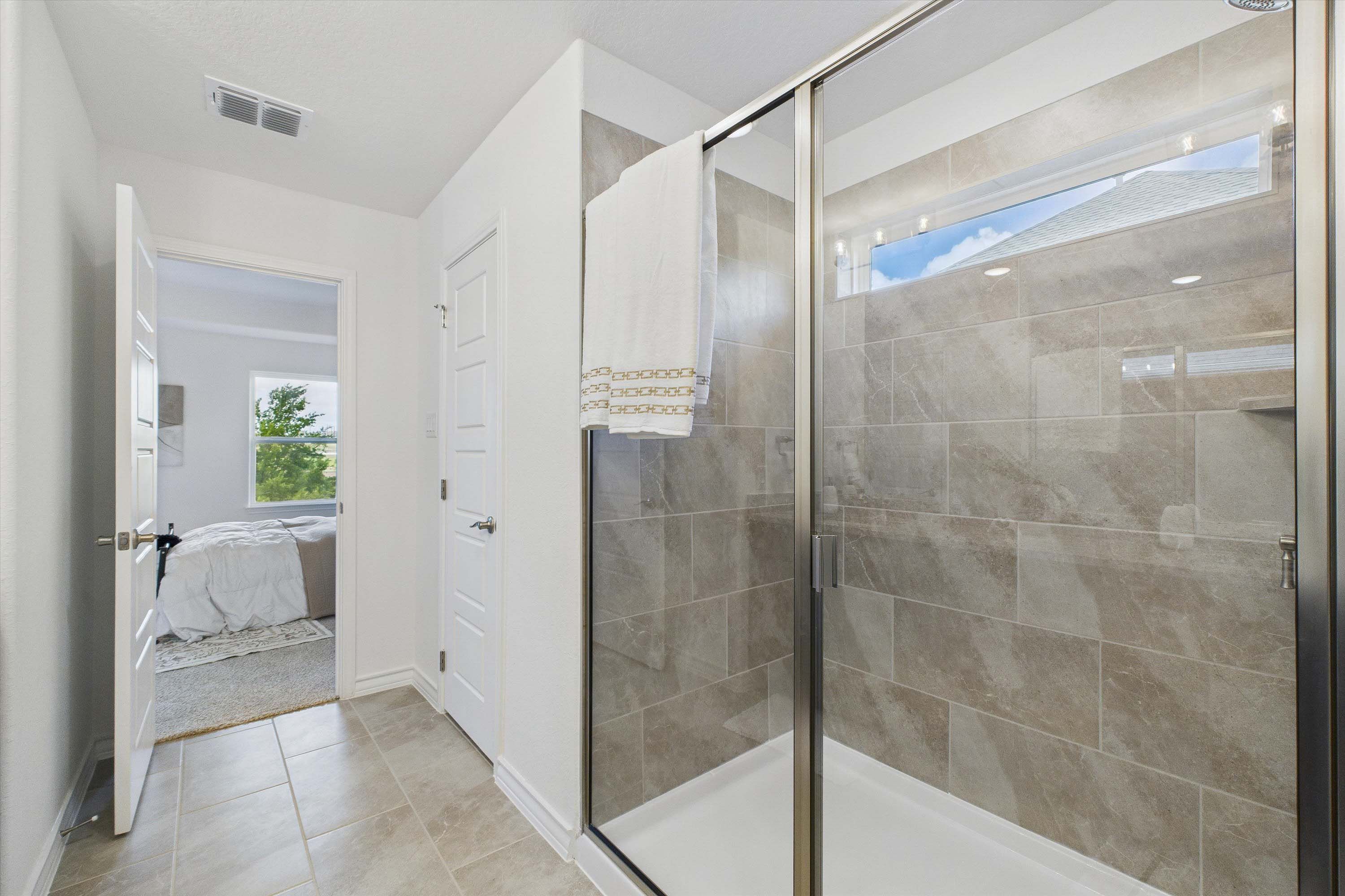 Walk-in shower with tile surround in The Danbury master suite, featuring a view into the bedroom.