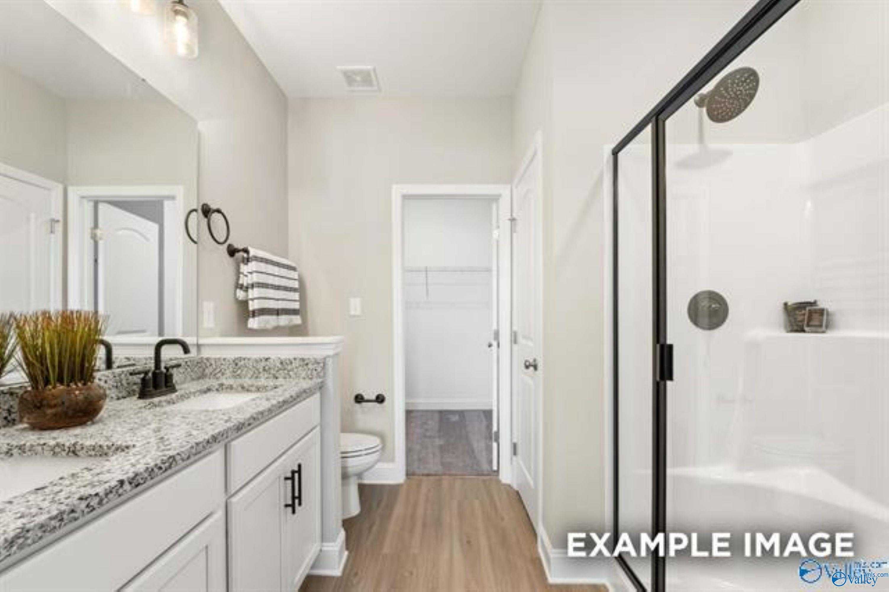 Modern bathroom with white quartz vanity, frameless glass shower, and wood flooring in Davidson Homes The Asheville, Owens Cross Roads, Alabama