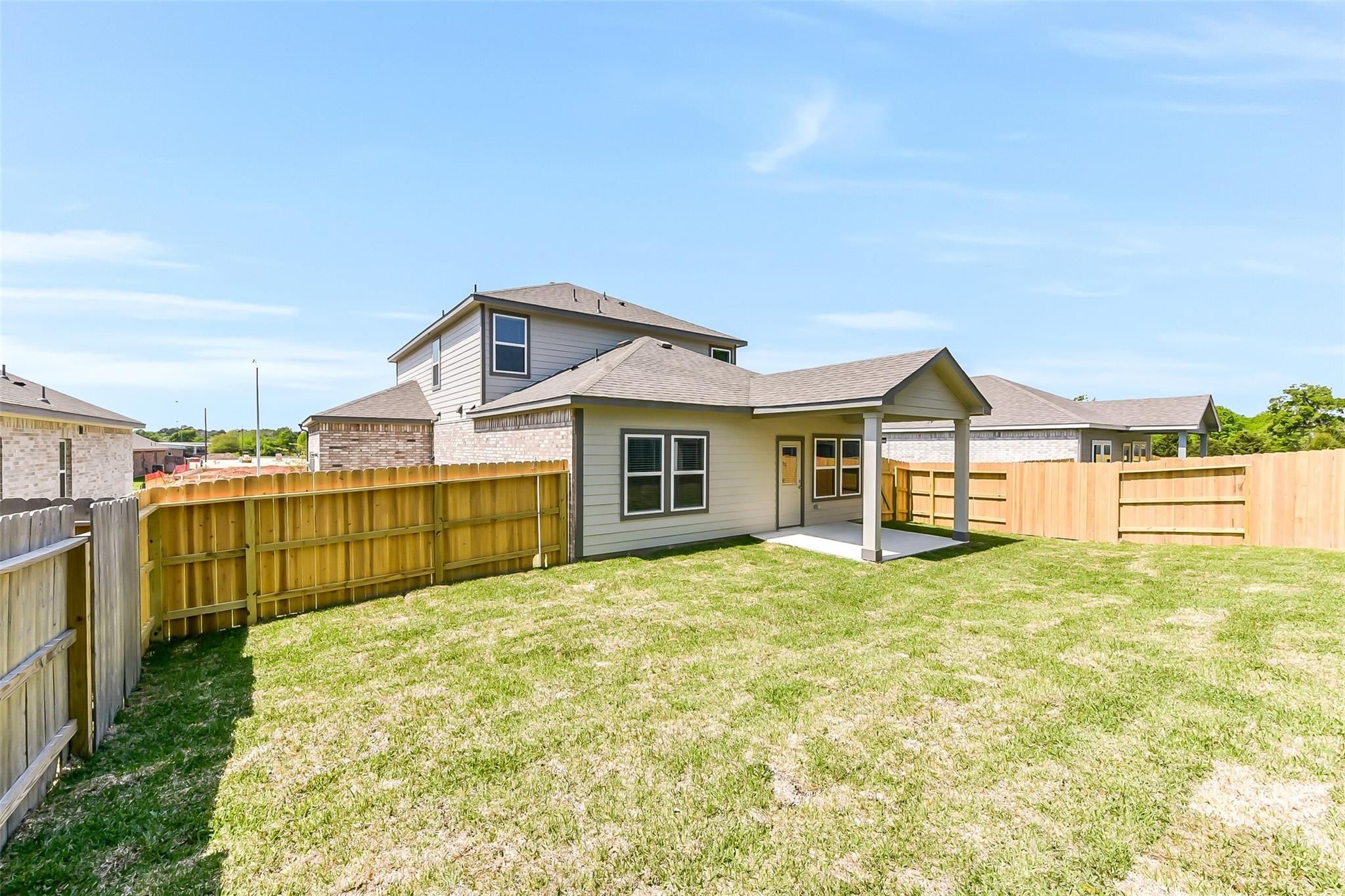 Private fenced backyard with lush green lawn behind two-story 5-bedroom Davidson Homes Brazos E in Windmill Estates, Magnolia, Texas