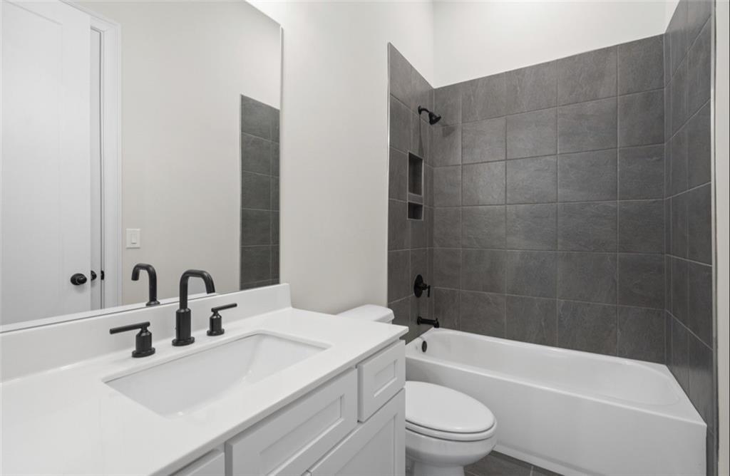Modern bathroom featuring white vanity, black fixtures, gray tile walk-in shower, and soaking tub in Davidson Homes The Seaside A, Woodstock, GA