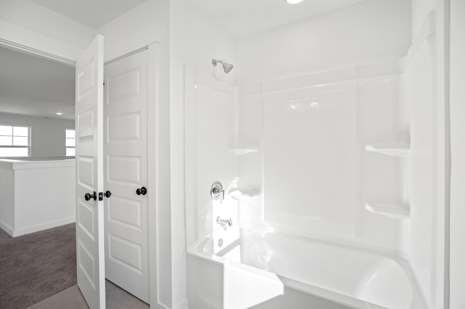 Bright white master bathroom with tub-shower combo, tiled walls, and open doors in Davidson Homes The Willow C, Gallatin, TN
