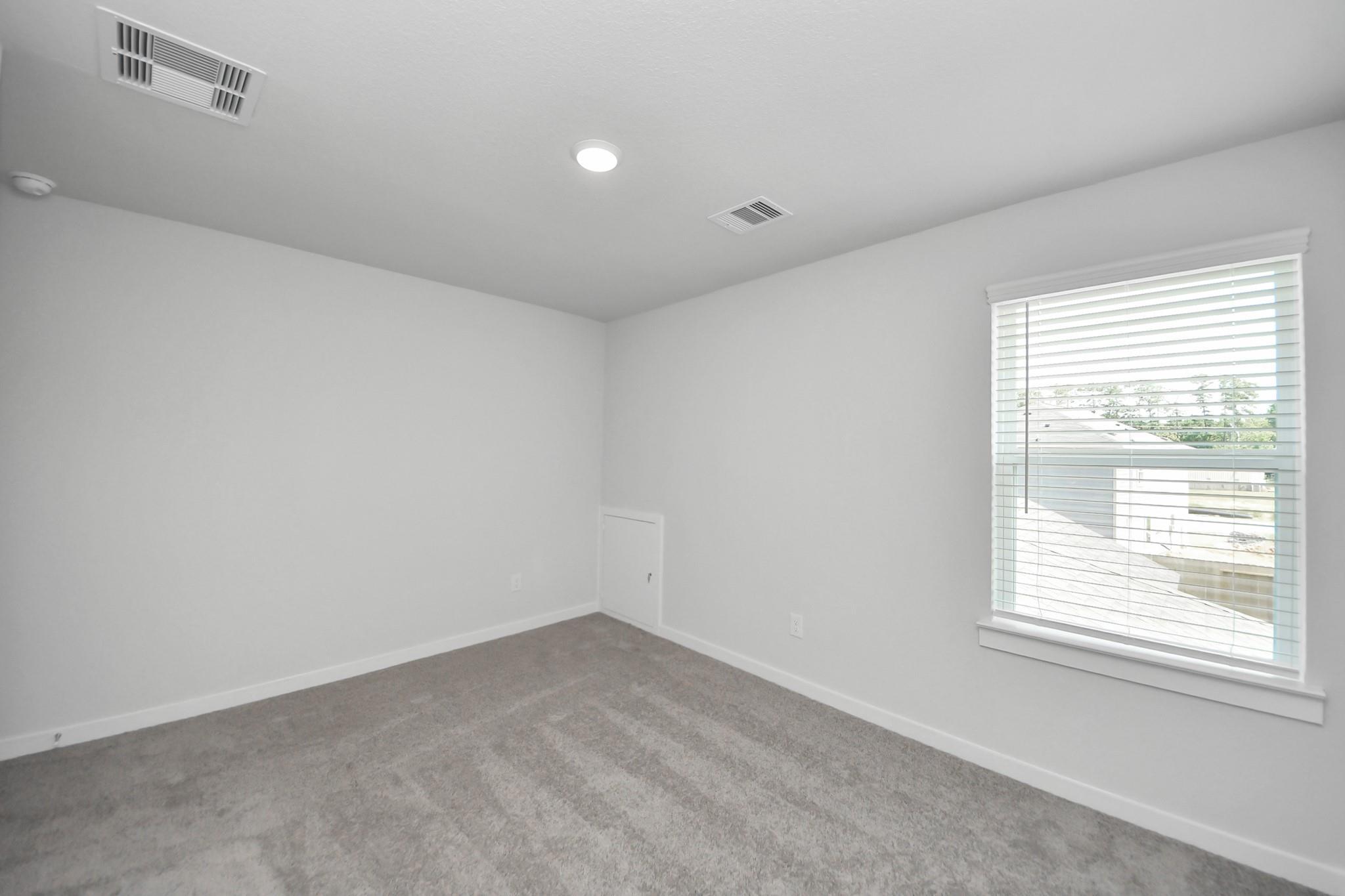 Spacious, carpeted bedroom with white walls and natural lighting in The Brazos F floor plan at Liberty Estates, Cleveland.