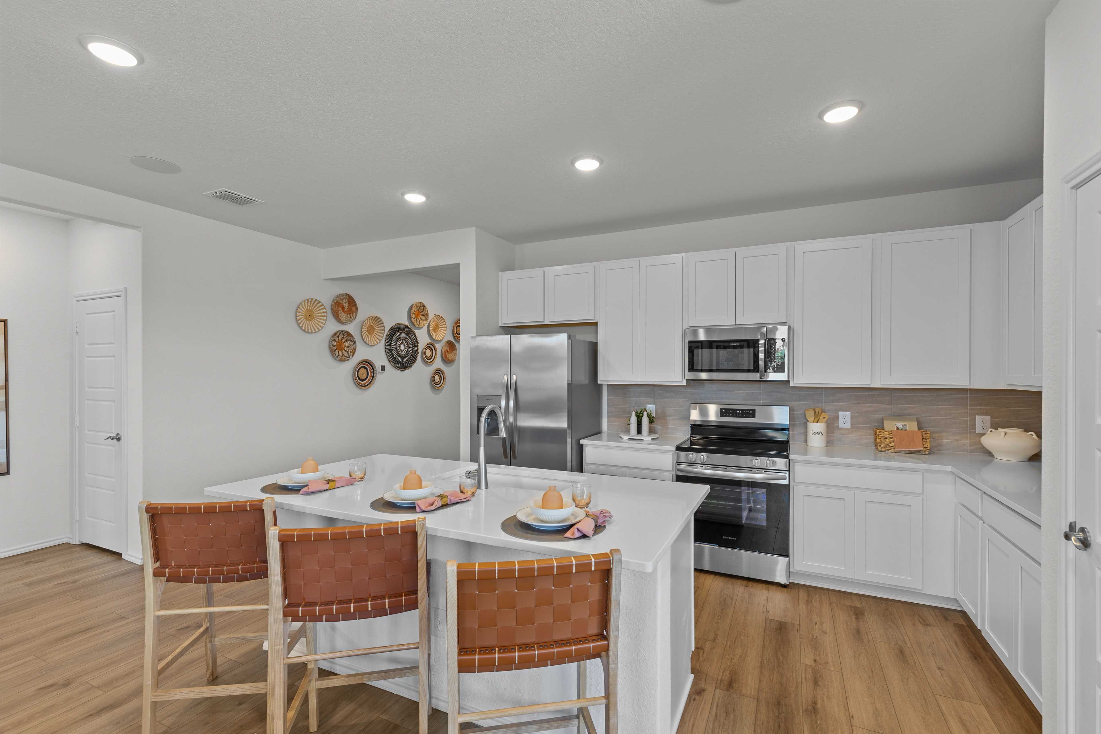Bright kitchen in The Daphne H with white shaker cabinets, stainless steel appliances, large island, leather bar stools, and woven wall decor
