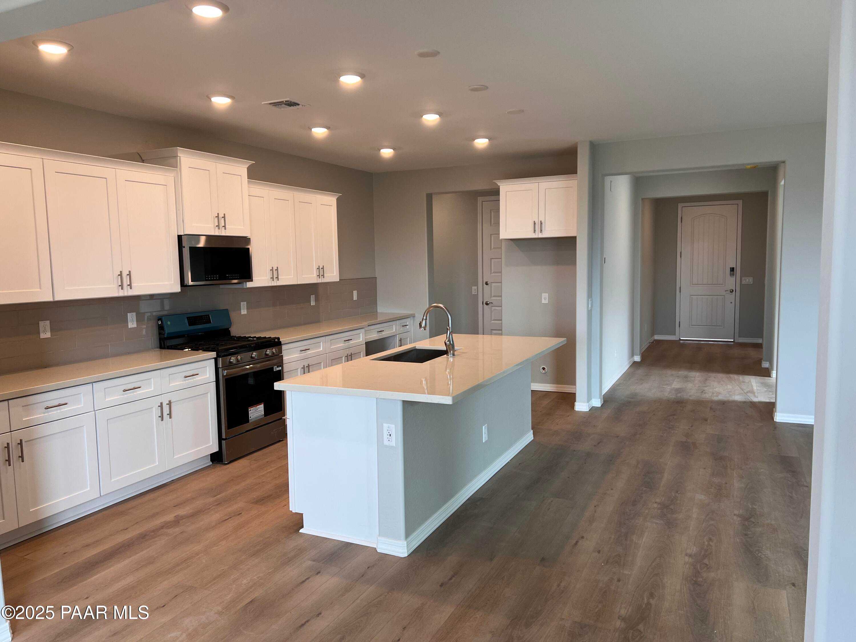 Modern open-concept kitchen featuring white shaker cabinets, stainless steel appliances, quartz island with sink in Davidson Homes Inspiration B, Prescott Valley, AZ
