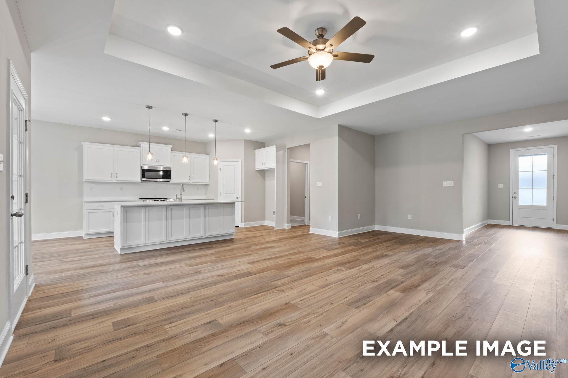 Open-concept kitchen with white cabinets, island, stainless appliances, and ceiling fan in The Montgomery 3-bedroom home, Meridianville, Alabama