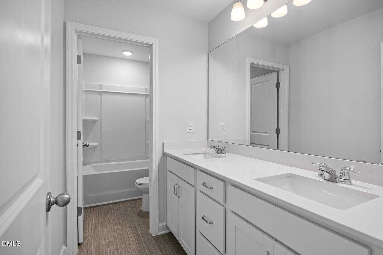 Bright white guest bathroom with single vanity, tub-shower combo, and modern mirror in The Hickory II B, Zebulon, NC