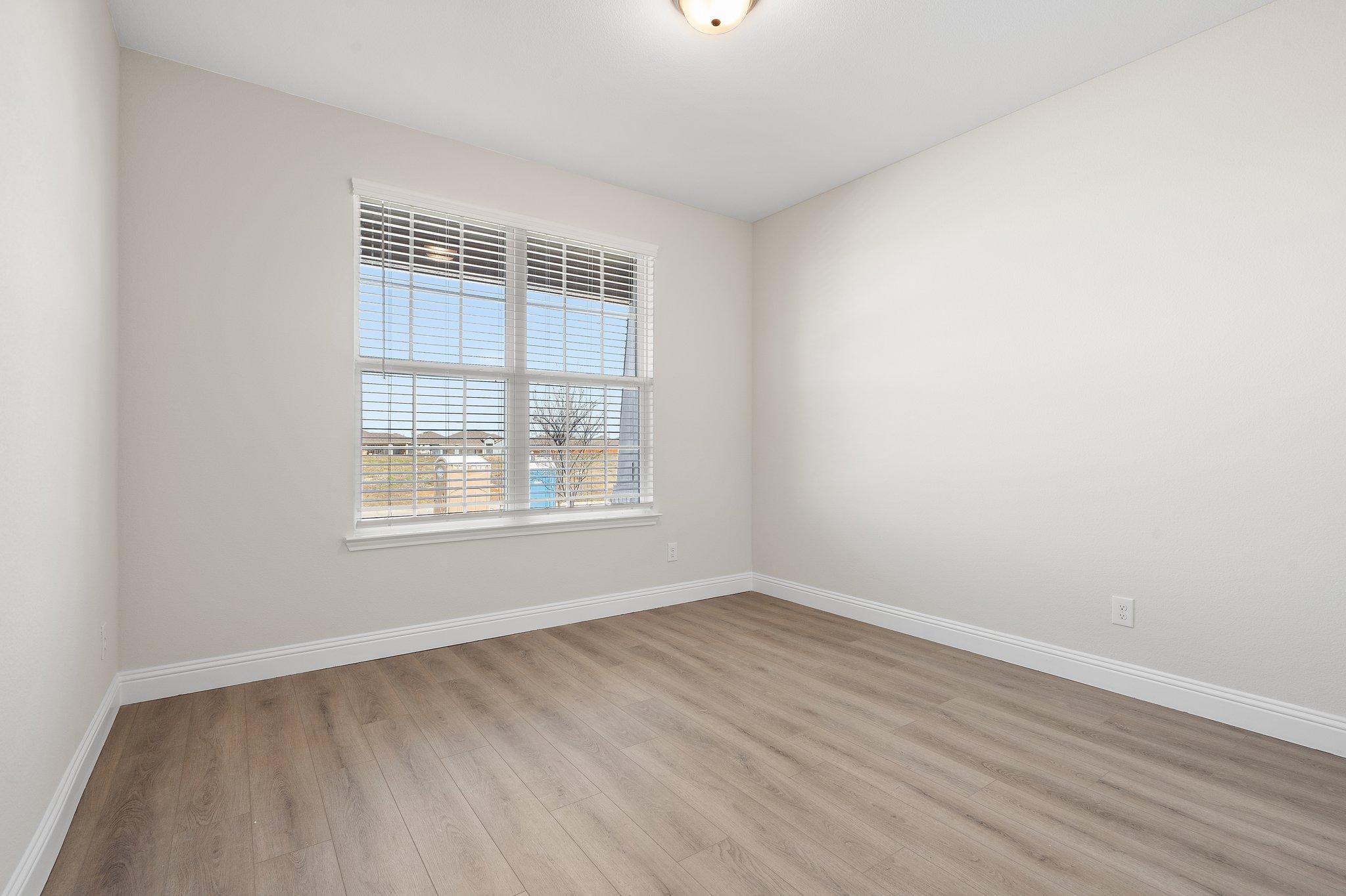 Bright bedroom with wood-look flooring and large window in The Holly floor plan by Davidson Homes in San Antonio, Texas.