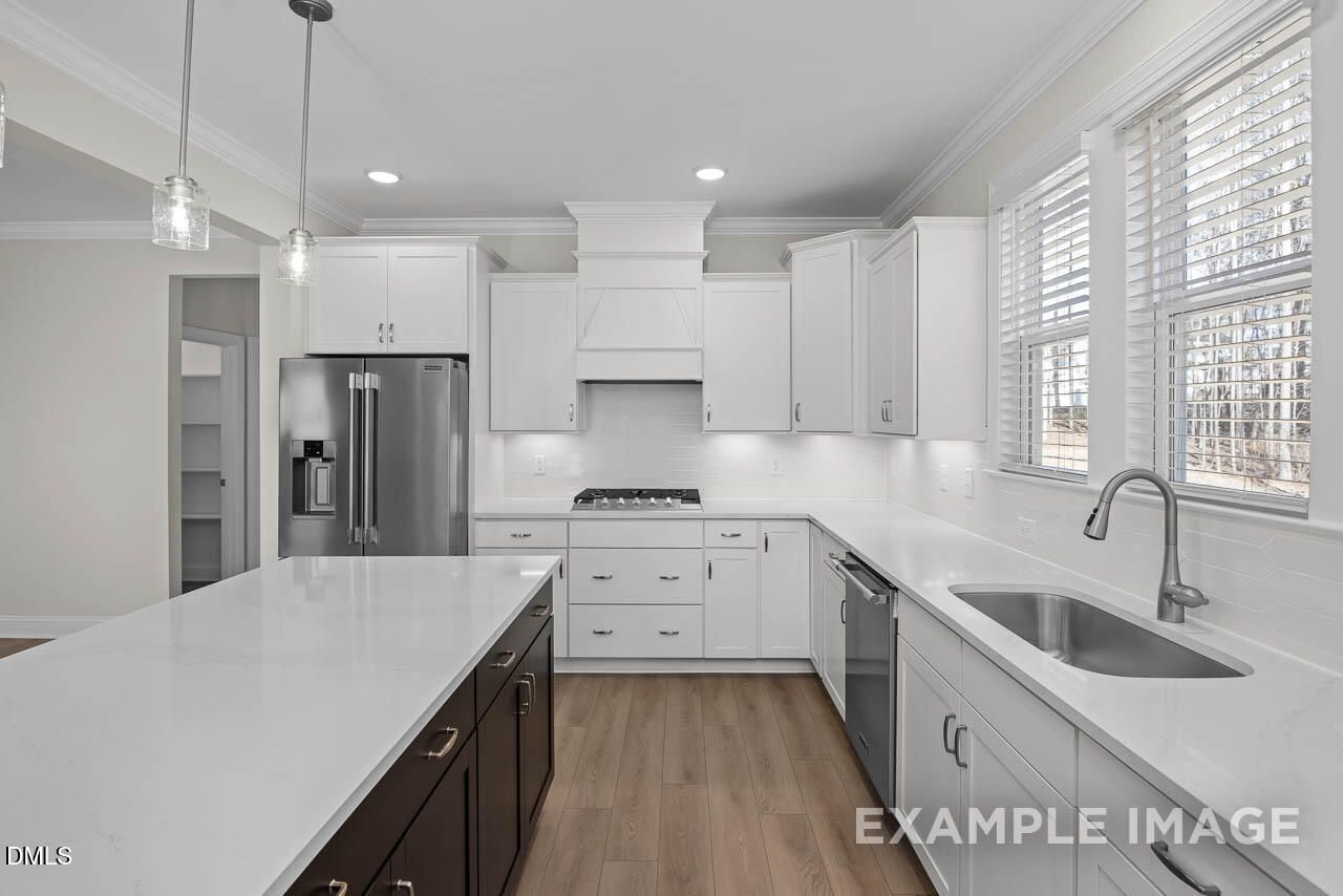 Modern white shaker kitchen with quartz island, stainless steel appliances, and hardwood floors in The Aspen C home, Apex, NC