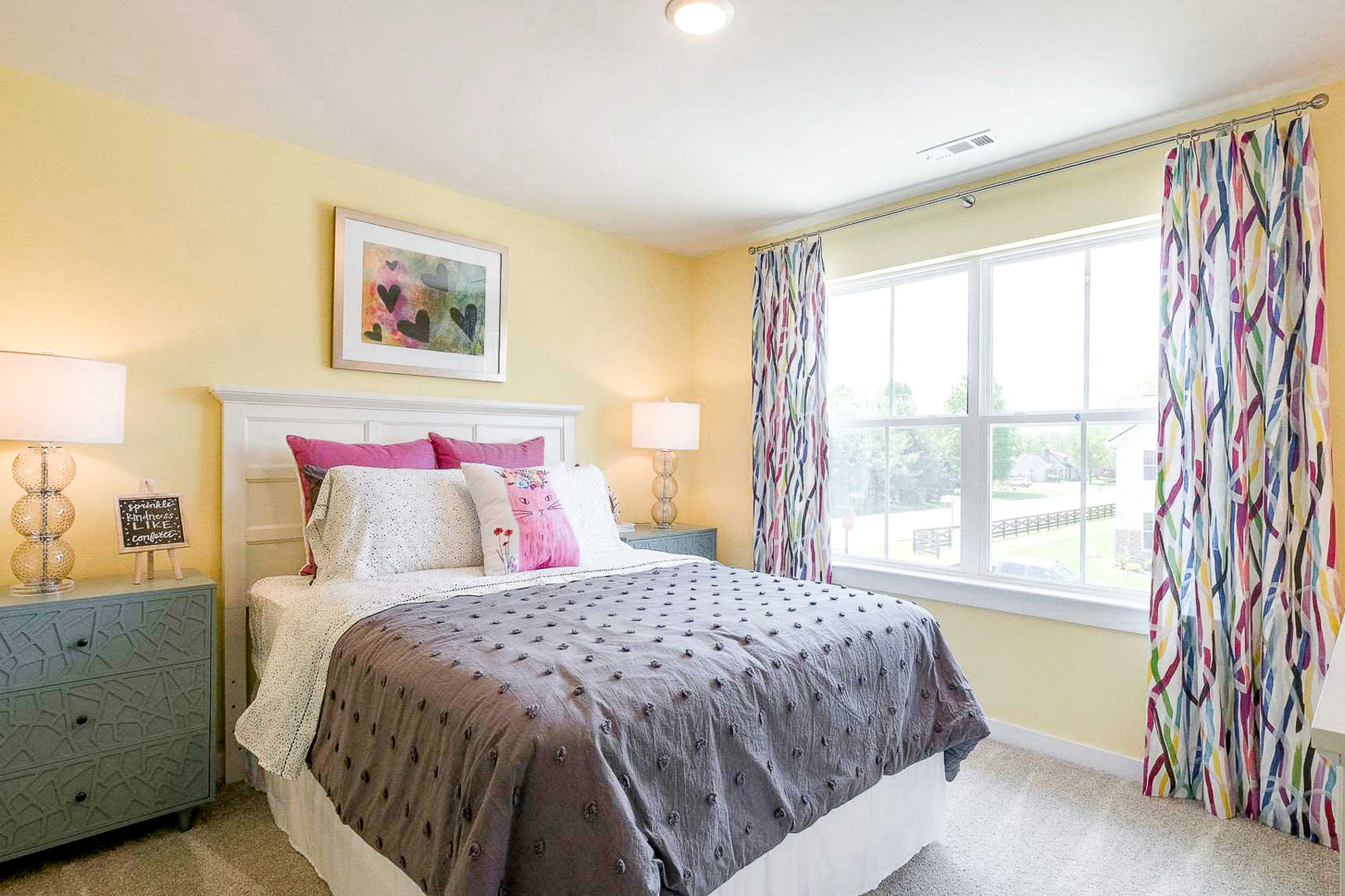 Cozy yellow bedroom with gray bed, pink pillows, and colorful curtains at The Meadows in Smyrna, Tennessee